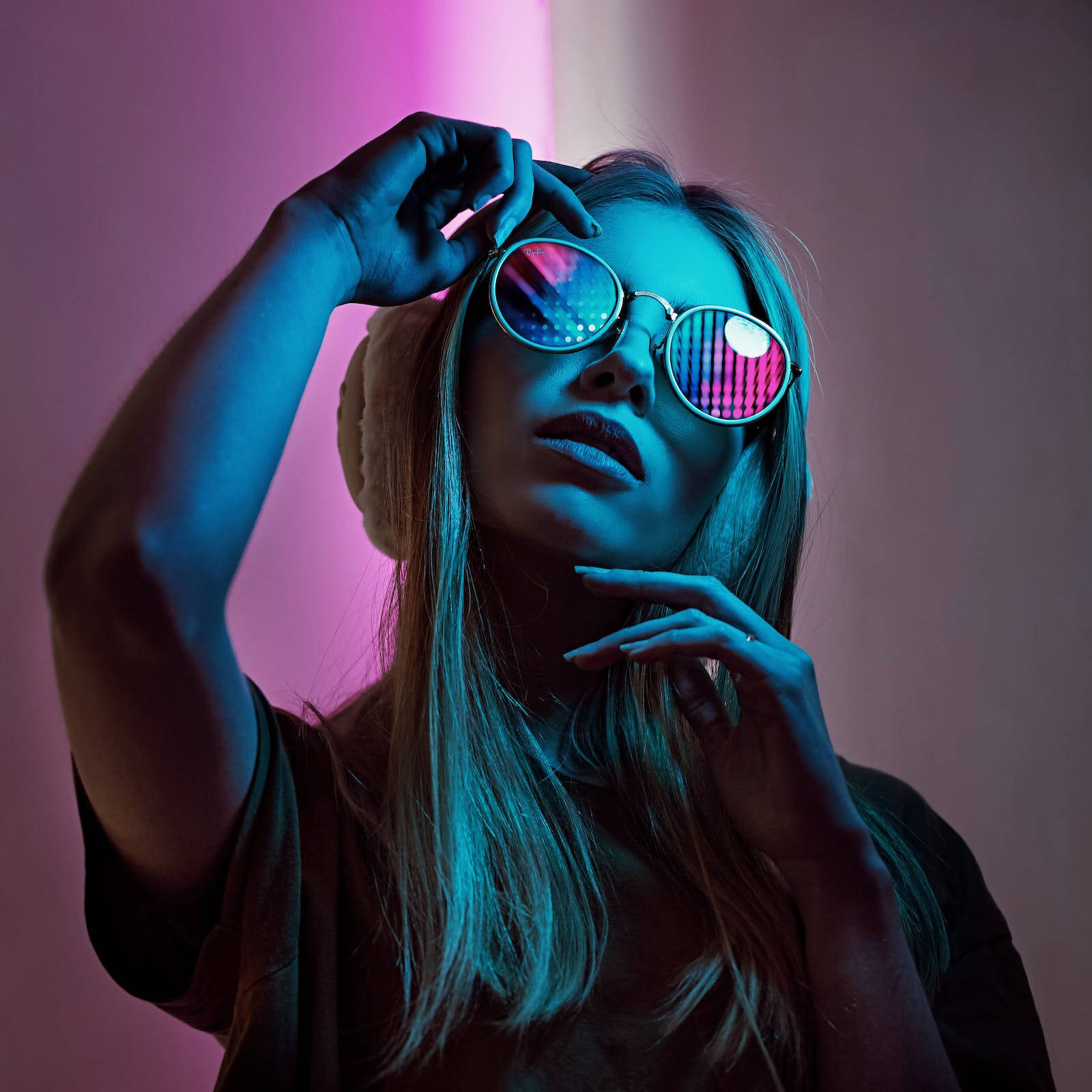 dark neon iPhone 桌布 壁紙 — 一位戴著發光霓虹太陽眼鏡和耳罩的女性，在充滿活力的粉紅色和藍色燈光牆前擺姿勢。