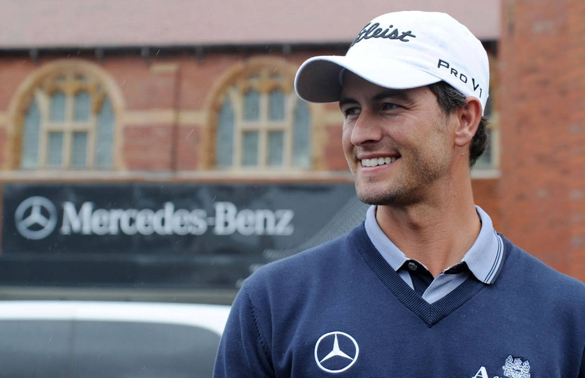 adam scott 桌布 壁紙 — 一位戴著白色帽子、身穿藍色毛衣的高爾夫球手微笑著站在Mercedes-Benz橫幅前，空氣中可見雨滴。