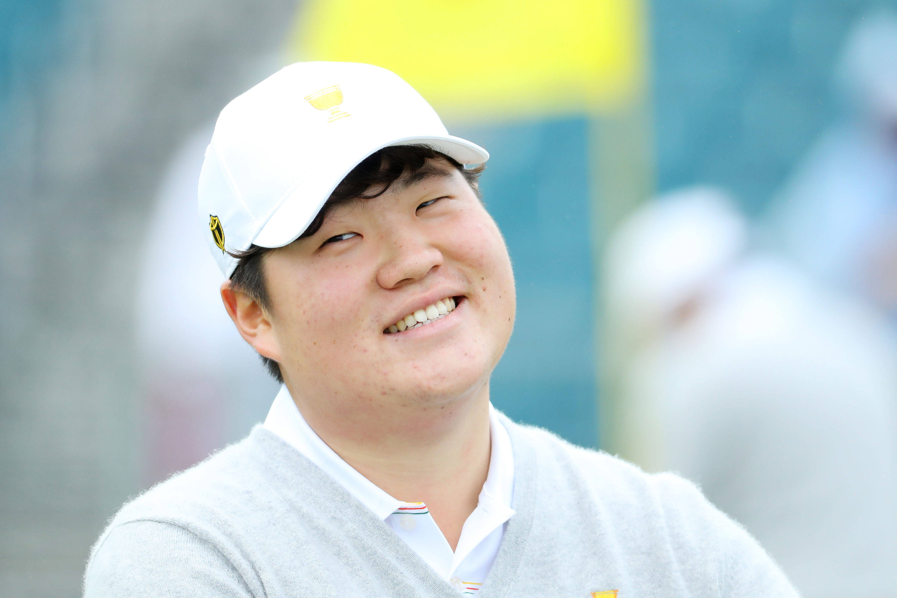 運動 桌布 壁紙 — 一位戴著白色帽子和灰色毛衣的高爾夫球手微笑著，在陽光明媚的戶外比賽中開心地向上看。