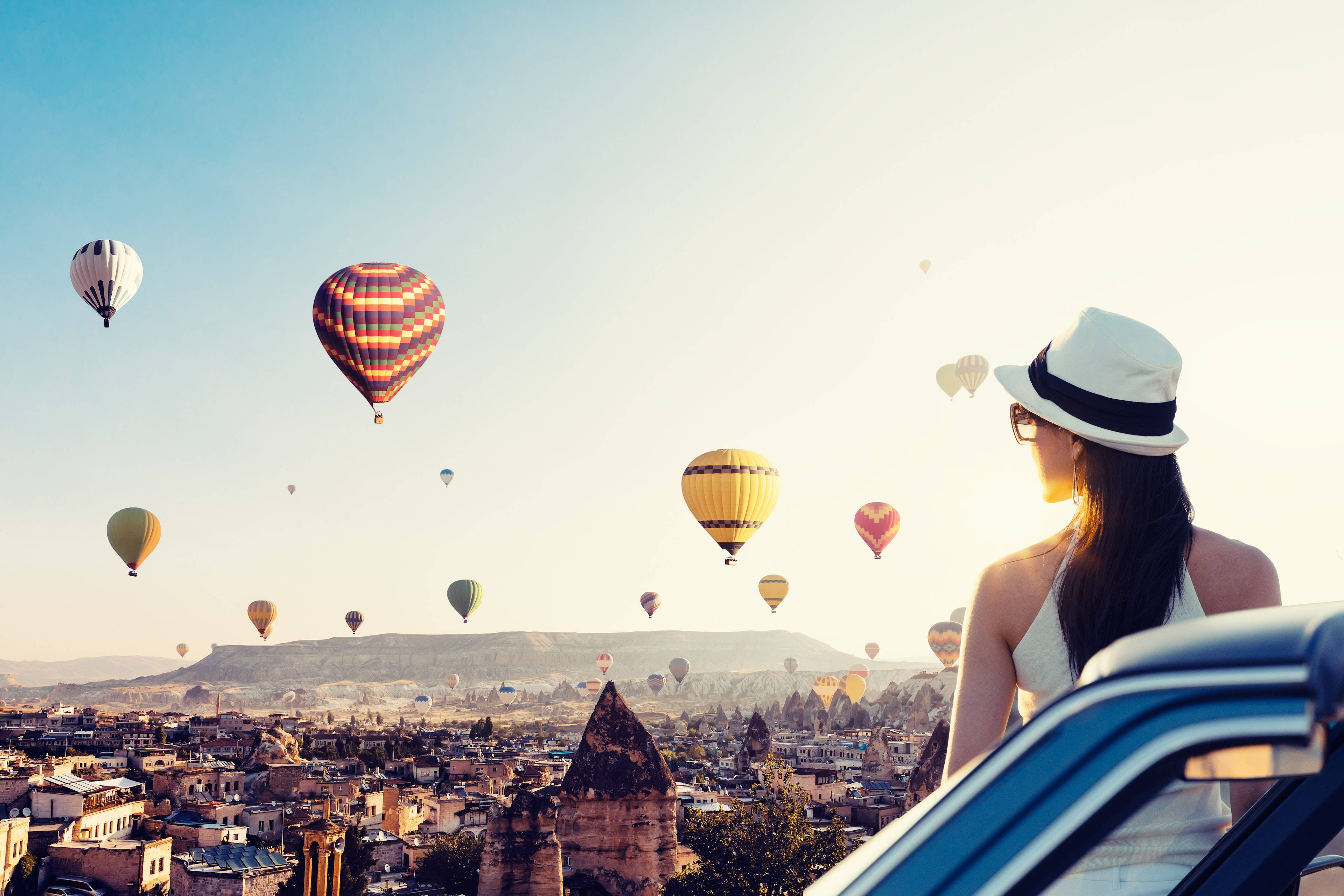 Cappadocia 桌布 壁紙 — 一位戴著白色帽子的女士在日出時分凝視著漂浮在卡帕多奇亞精靈煙囪上空的彩色熱氣球。