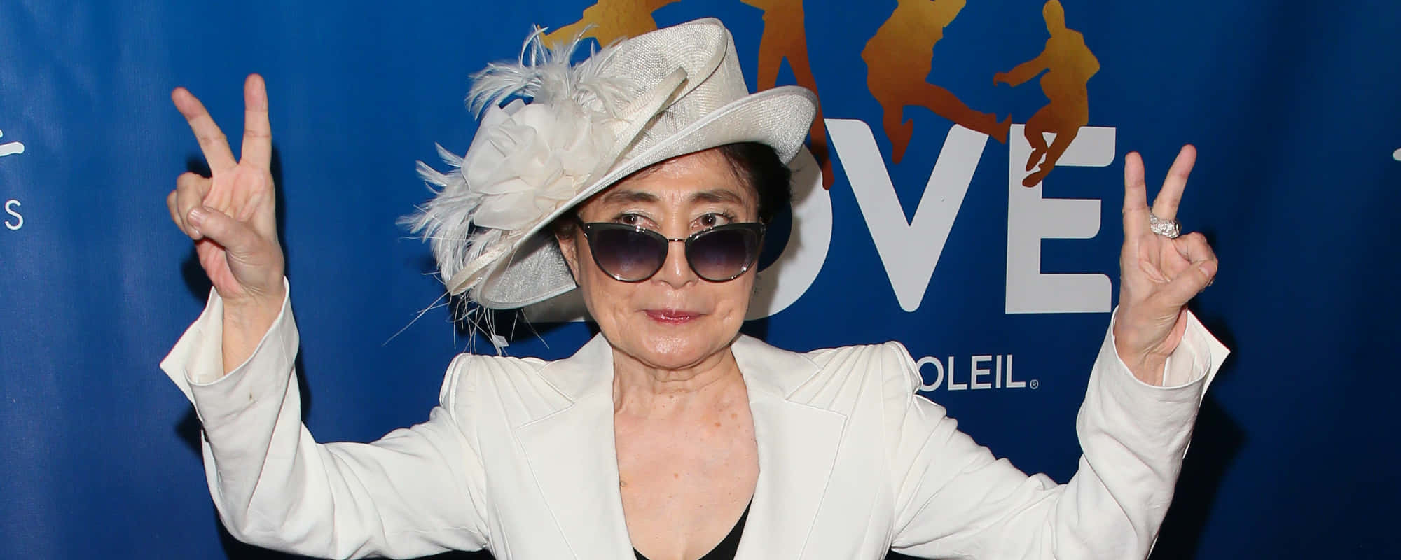 Sunglasses 桌布 壁紙 — 一位戴著白色羽毛帽和太陽眼鏡的女性，在帶有金色剪影的藍色活動背景前比出和平手勢。