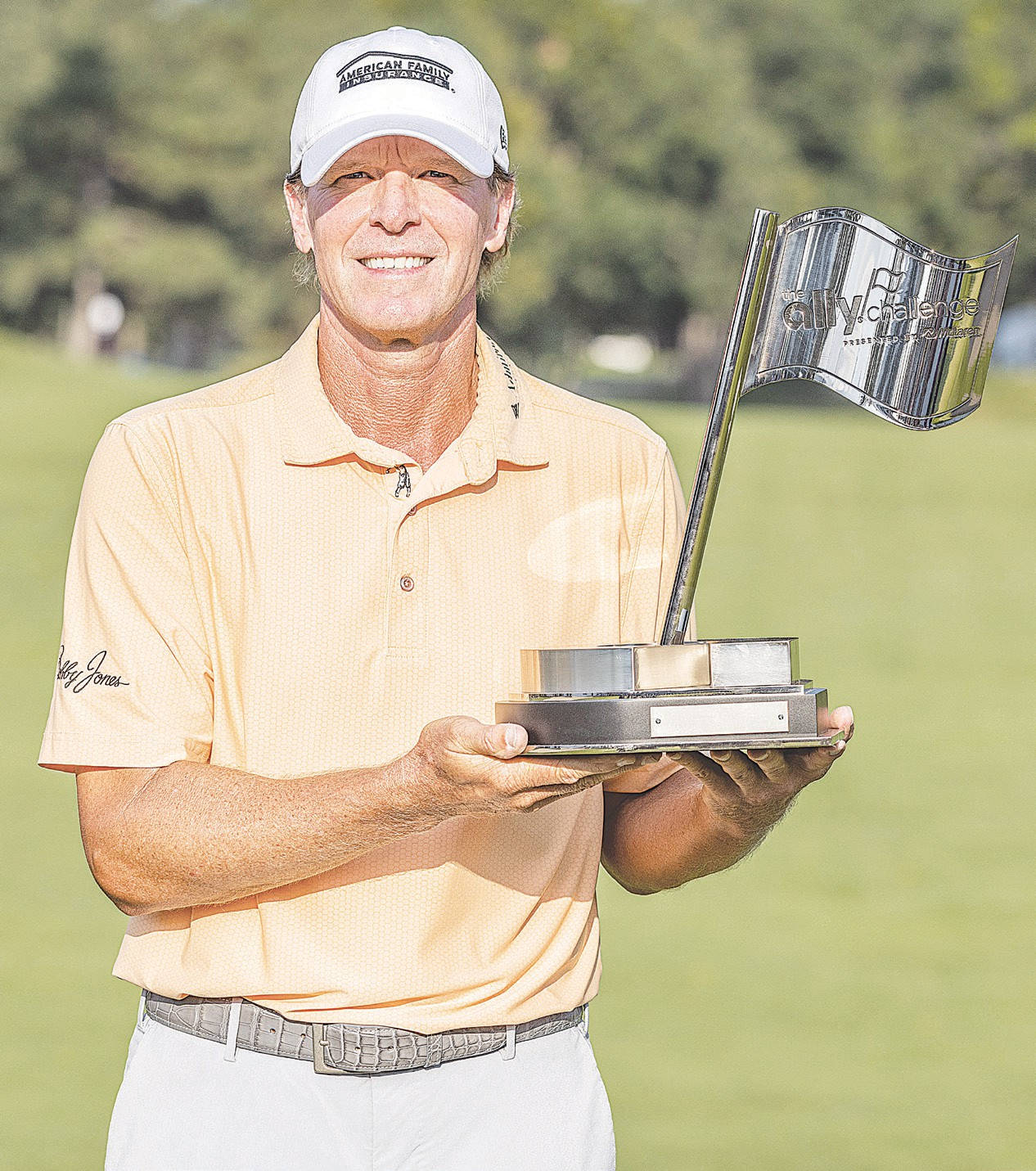 Trophy 桌布 壁紙 — 一位戴著白色鴨舌帽、身穿蜜桃色Polo衫的高爾夫球手，在陽光明媚的高爾夫球場上自豪地高舉一面帶有旗幟的銀色獎盃。