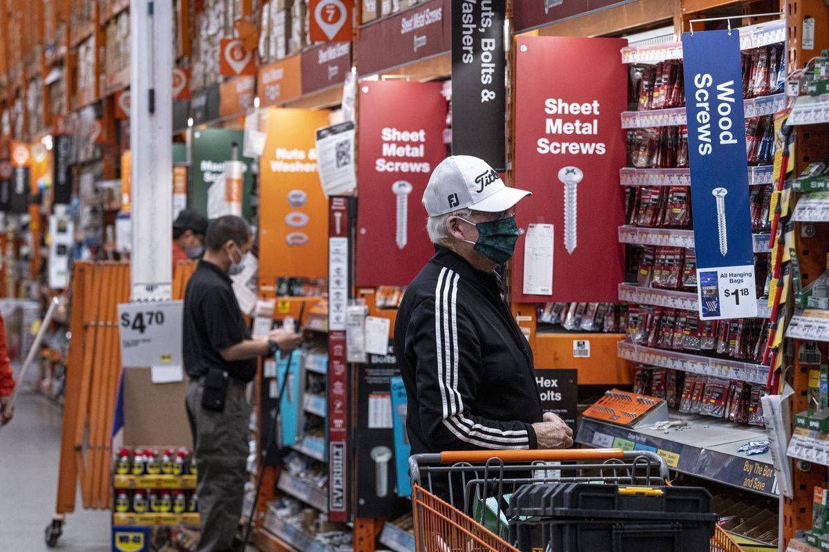 Home Depot 桌布 壁紙 — 一位戴著白色鴨舌帽和口罩的長者，在燈光明亮的五金店內瀏覽貨架，貨架上擺滿了螺絲和螺栓。