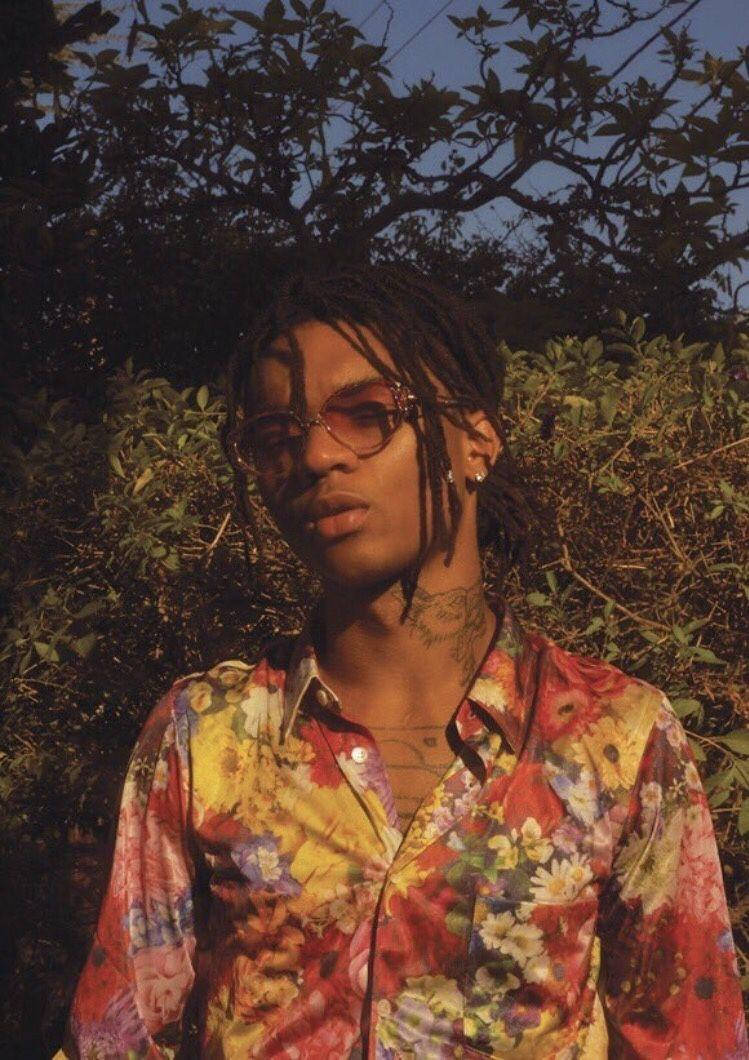 Swae Lee 桌布 壁紙 — 一位戴著眼鏡、留著辮子頭的年輕男子，在金色時光的光線下，以茂密的樹葉為背景，穿著一件鮮豔的花襯衫。