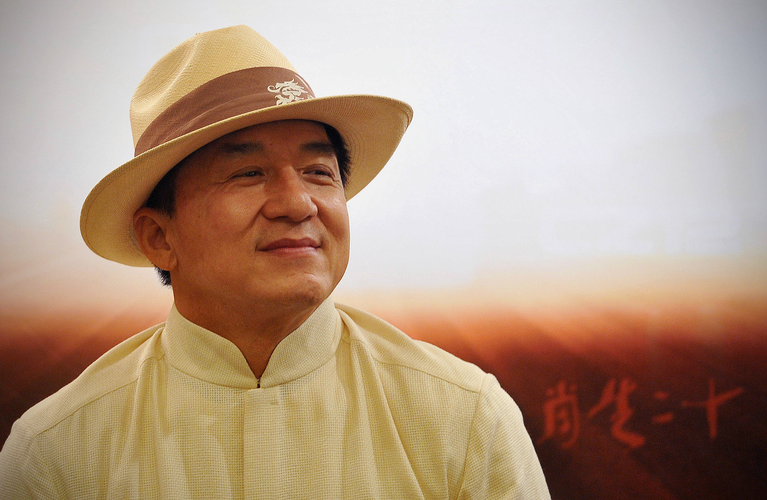 漸層 桌布 壁紙 — 一位戴著米色帽子、穿著相配襯衫的男子，在柔和日落背景下，伴隨著中文字，溫暖地微笑。