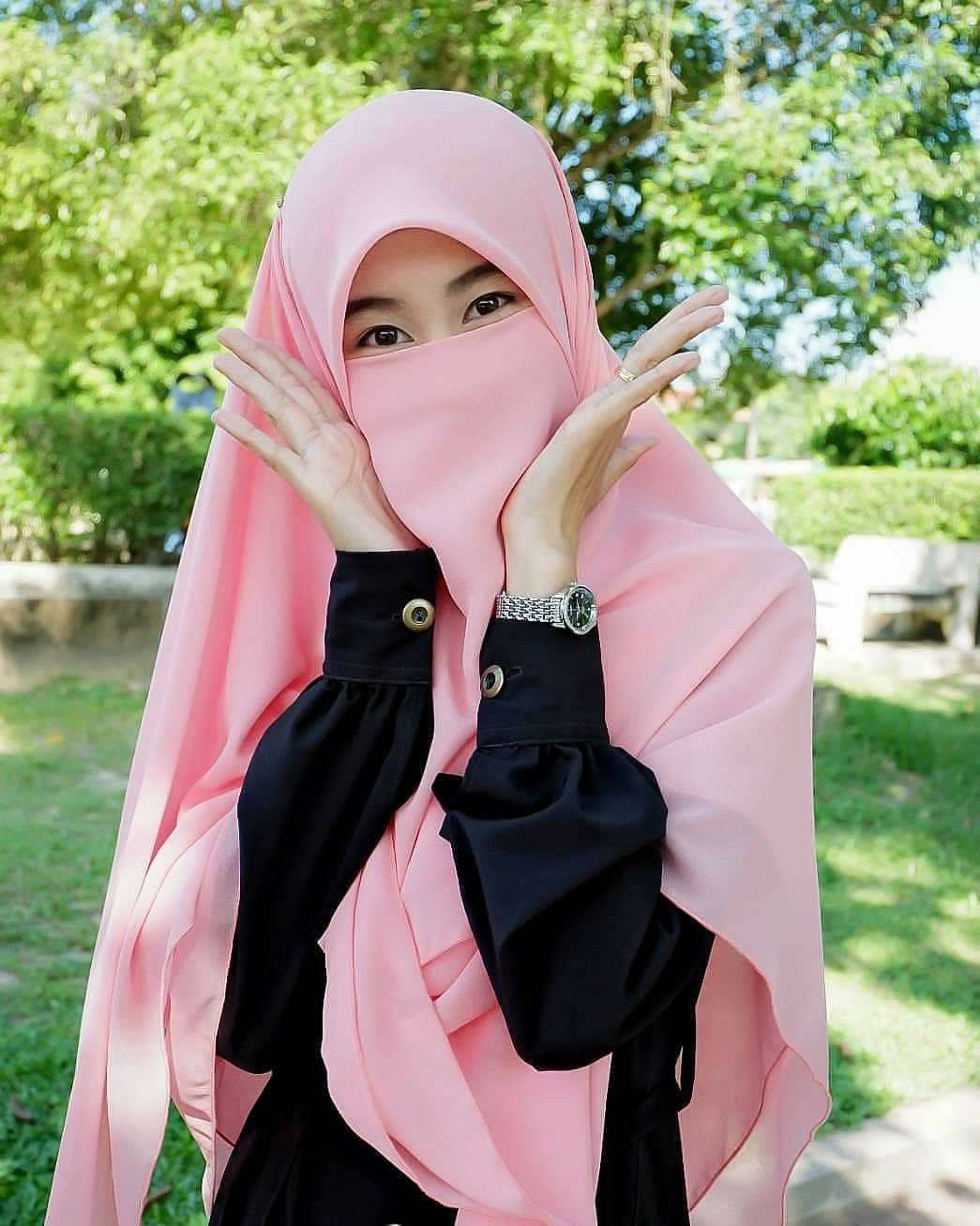muslim 桌布 壁紙 — 一位戴著粉紅色頭巾、身穿黑色襯衫的女性在陽光明媚的花園中頑皮地用手遮住臉。