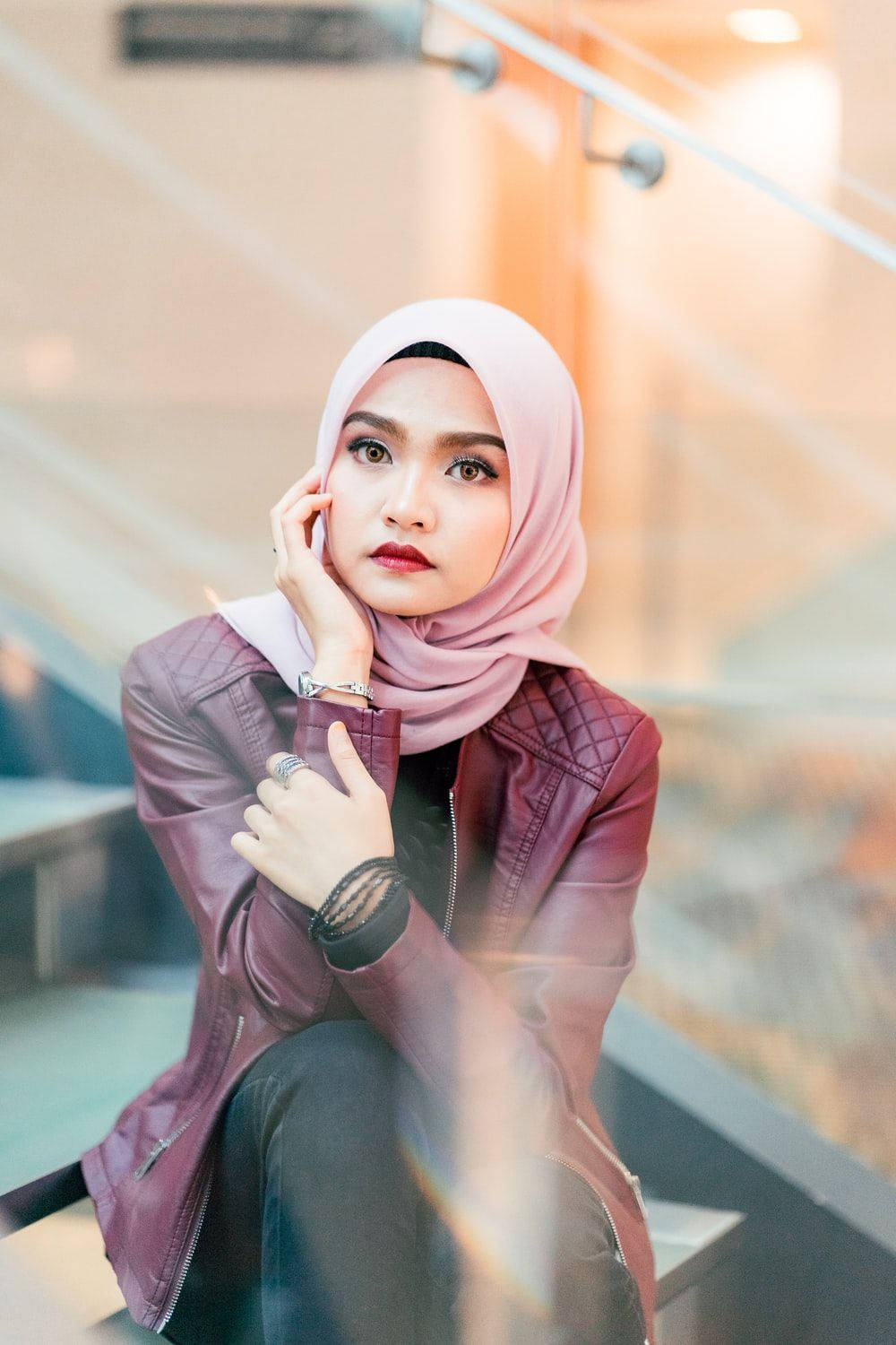 muslim 桌布 壁紙 — 一位戴著粉紅色頭巾和栗色皮夾克的女性，坐在柔和溫暖燈光的現代樓梯上沉思。