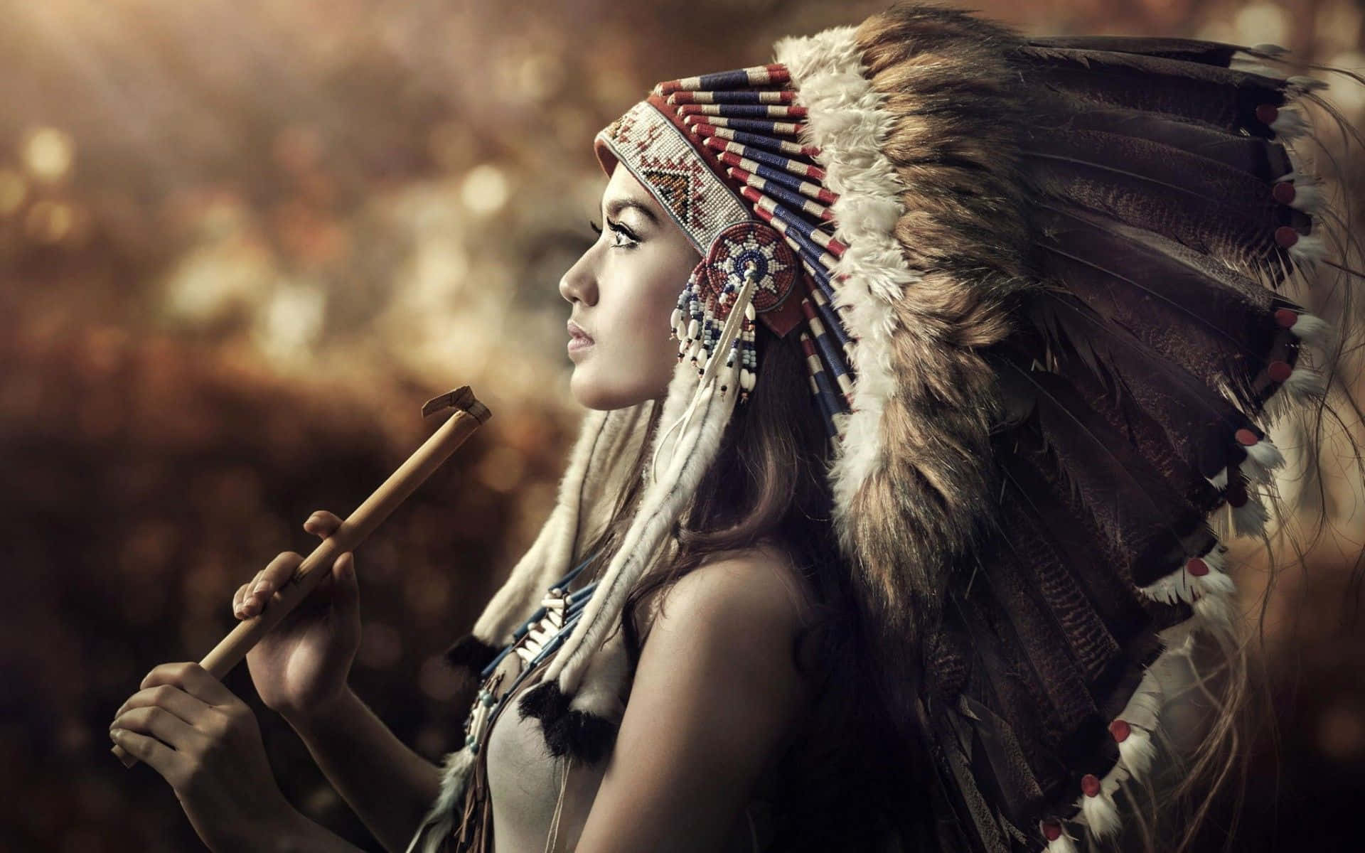 Tribal 桌布 壁紙 — 一位戴著精緻羽毛頭飾的女性，在溫暖模糊的背景中手持木杖。