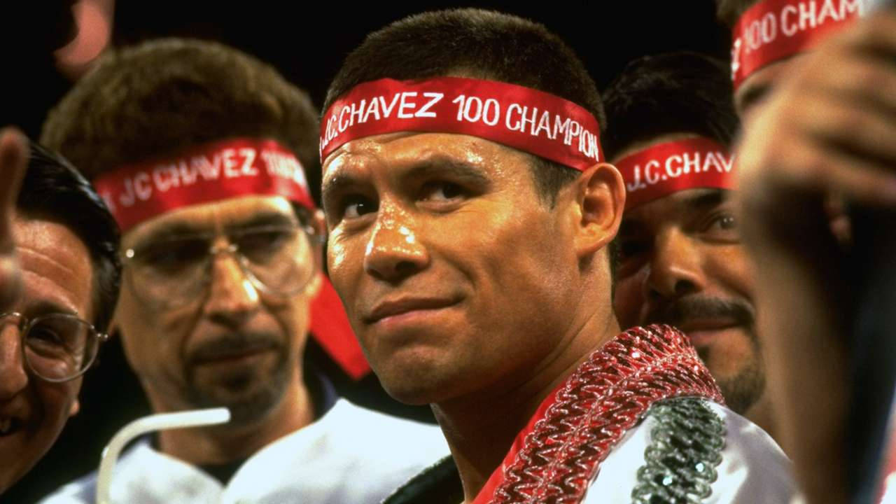 Handsome Man 桌布 壁紙 — 一位戴著紅色 'J.C. CHAVEZ 100 CHAMPION' 頭帶的勝利拳擊手，在燈光昏暗的競技場中，於歡呼的粉絲間微笑。