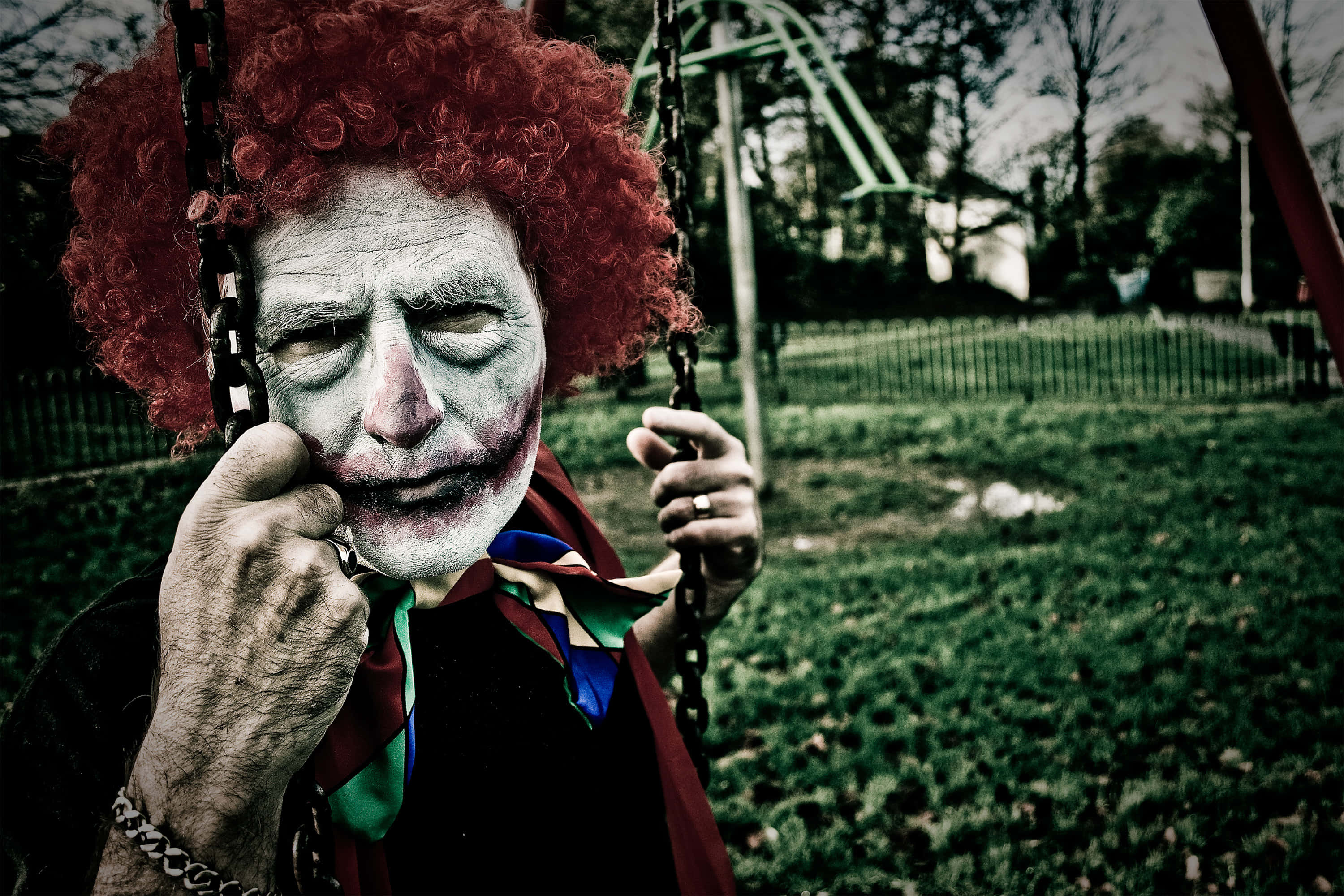 詭異的GIF 桌布 壁紙 — 一位戴著紅色假髮和小丑妝容的長者坐在公園的鞦韆上，用手托著臉，表情陰沉。