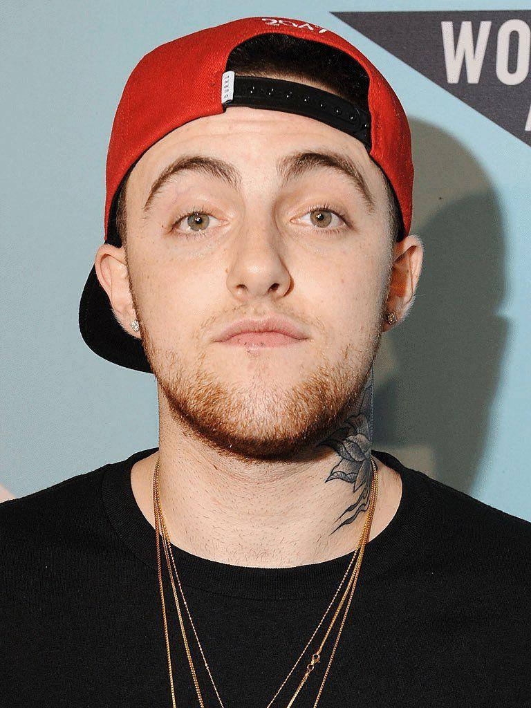 Mac Miller 桌布 壁紙 — 一位戴著紅色棒球帽和金鏈的年輕男子，在淺藍色背景下直視鏡頭。