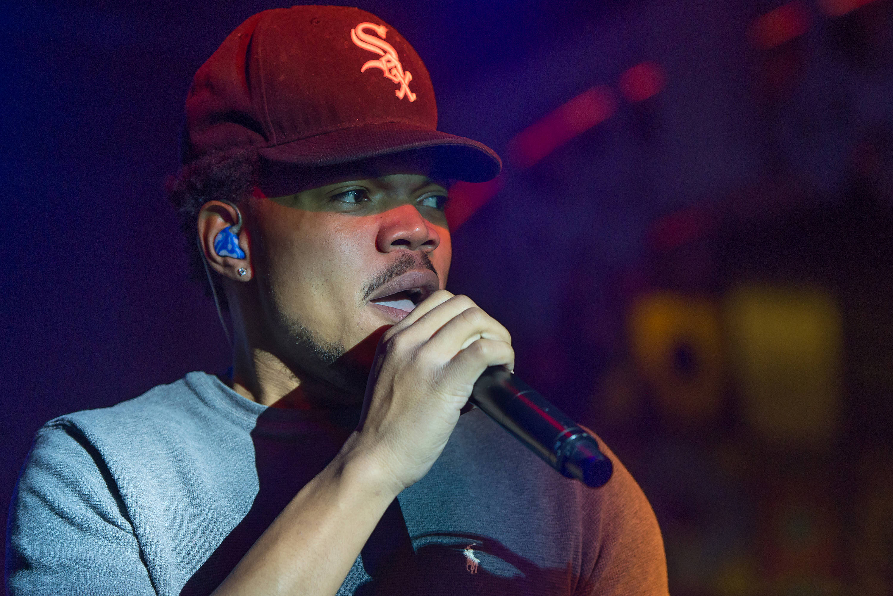 chance 桌布 壁紙 — 一位戴著紅色棒球帽的男饒舌歌手在充滿活力的舞台燈光下對著麥克風唱歌。