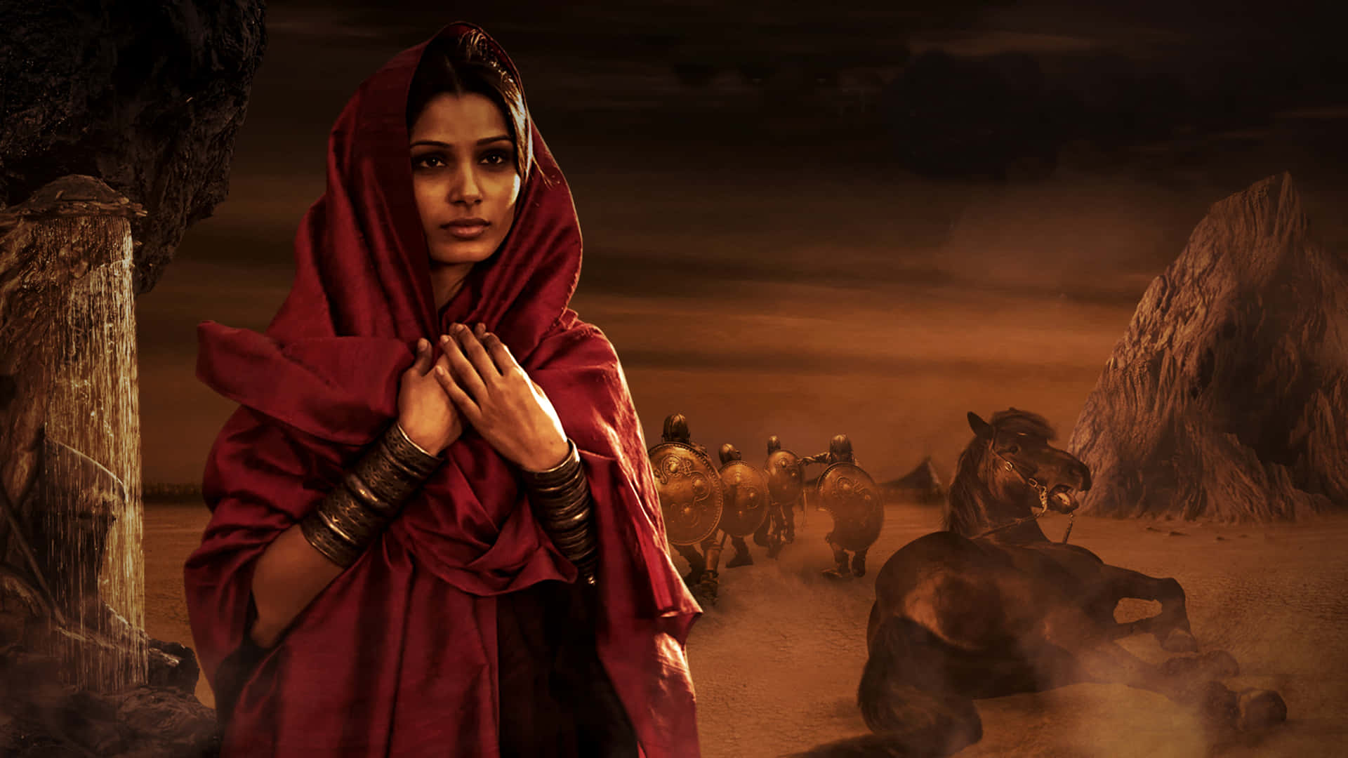 Freida Pinto 桌布 壁紙 — 一位戴著紅色面紗的女子莊嚴地站在沙漠中，背景中裝甲騎手和馬匹在昏暗的天空下移動。