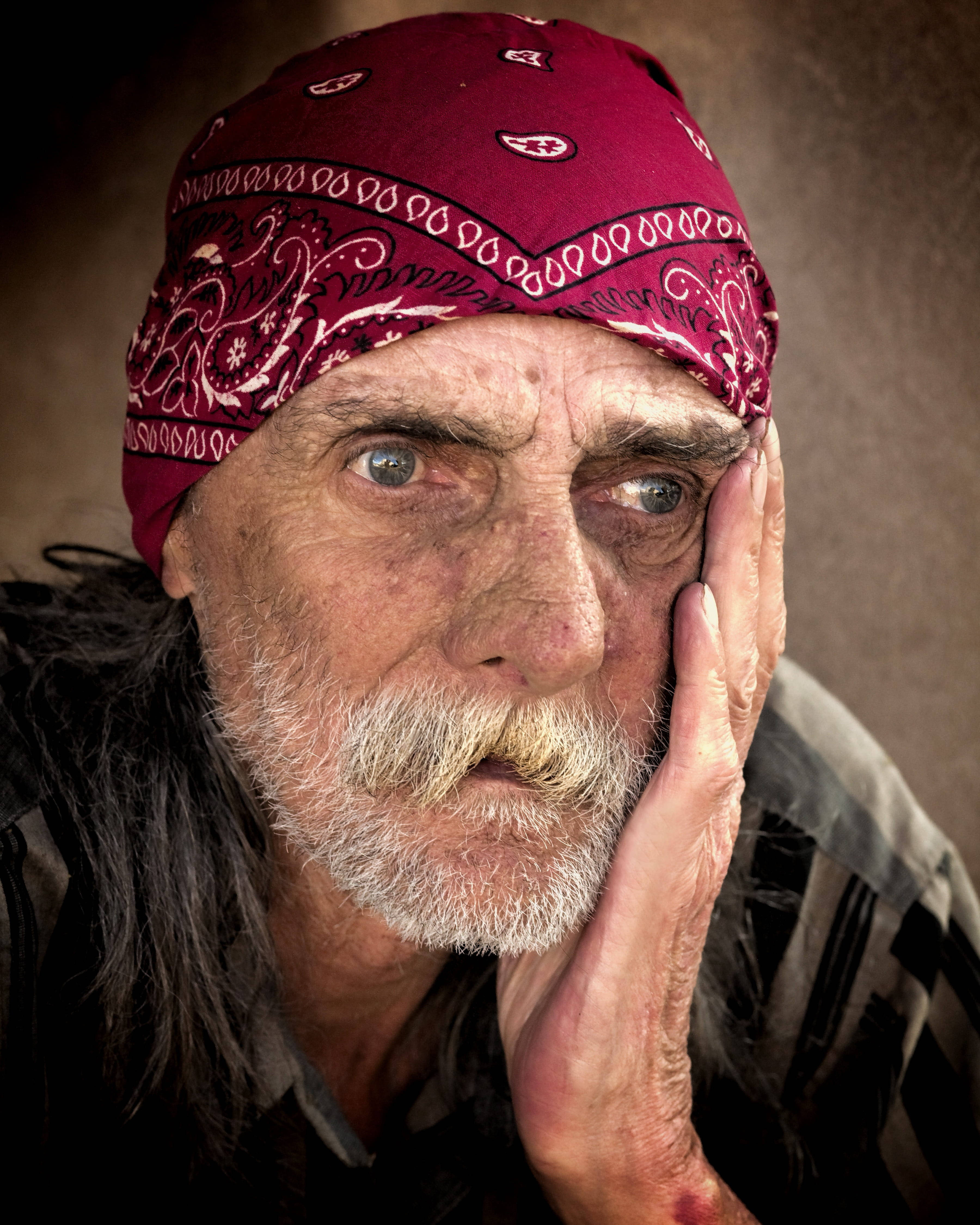 Man Face 桌布 壁紙 — 一位戴著紅色頭巾、面容滄桑的長者，將手放在臉頰上的特寫肖像。