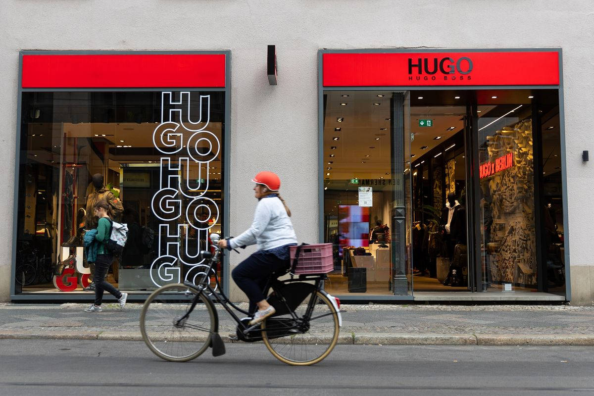 Clothes 桌布 壁紙 — 一位戴著紅色頭盔的自行車騎士騎過一間Hugo Boss商店，商店有醒目的紅色招牌和玻璃窗，反映城市生活。