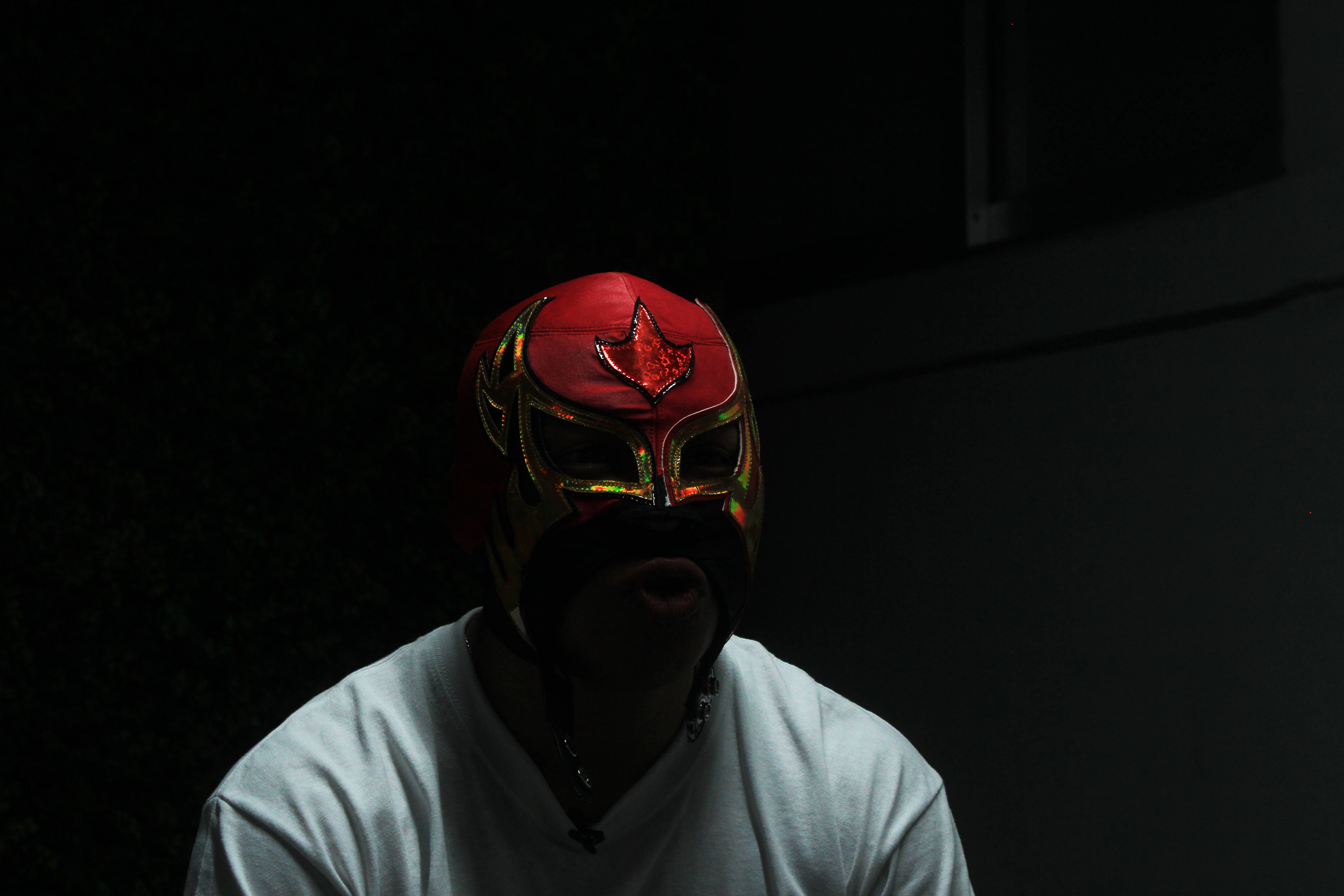 Nacho Libre 桌布 壁紙 — 一位戴著紅金面具的摔角手在昏暗光線下對著黑暗背景凝視。