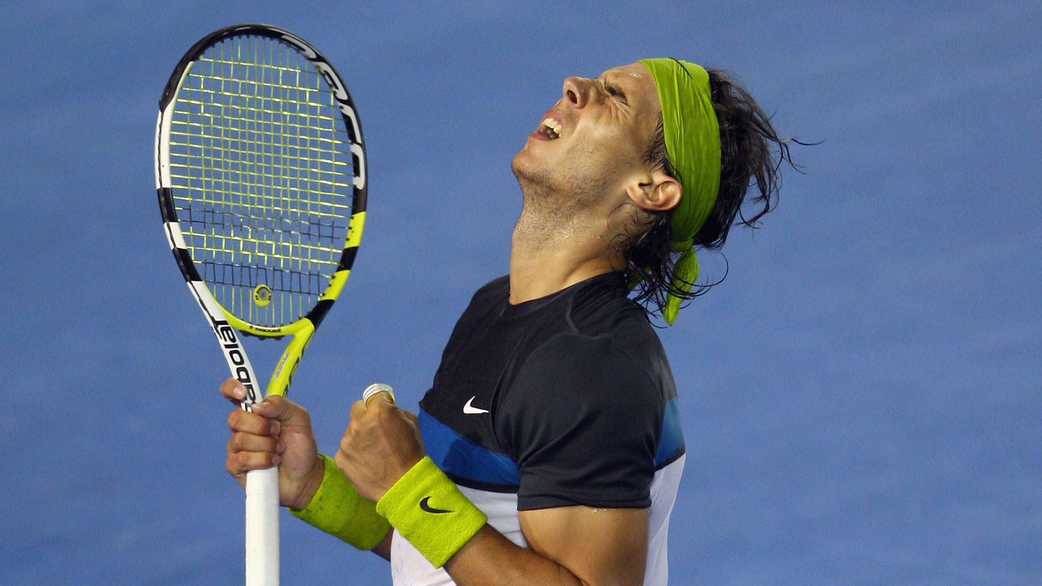 Tennis 桌布 壁紙 — 一位戴著綠色頭帶和護腕的網球選手，在藍色球場背景下高舉球拍，勝利慶祝。