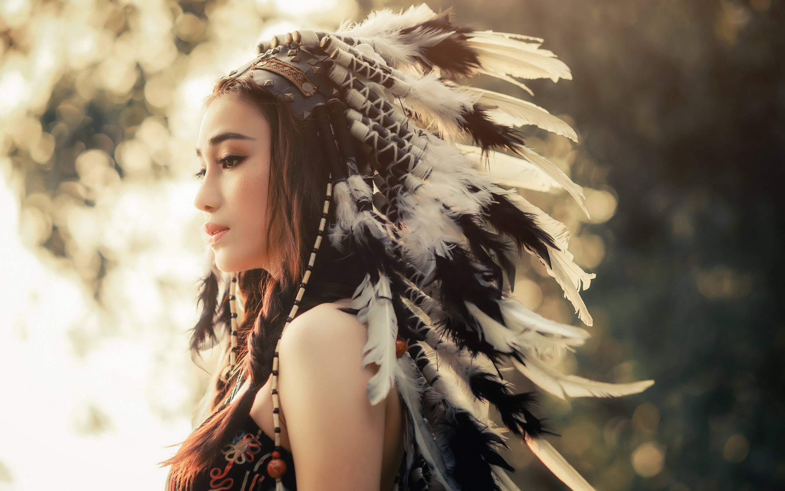 美女 桌布 壁紙 — 一位戴著羽毛頭飾的女性，在陽光普照、模糊的森林背景下若有所思地凝視著。