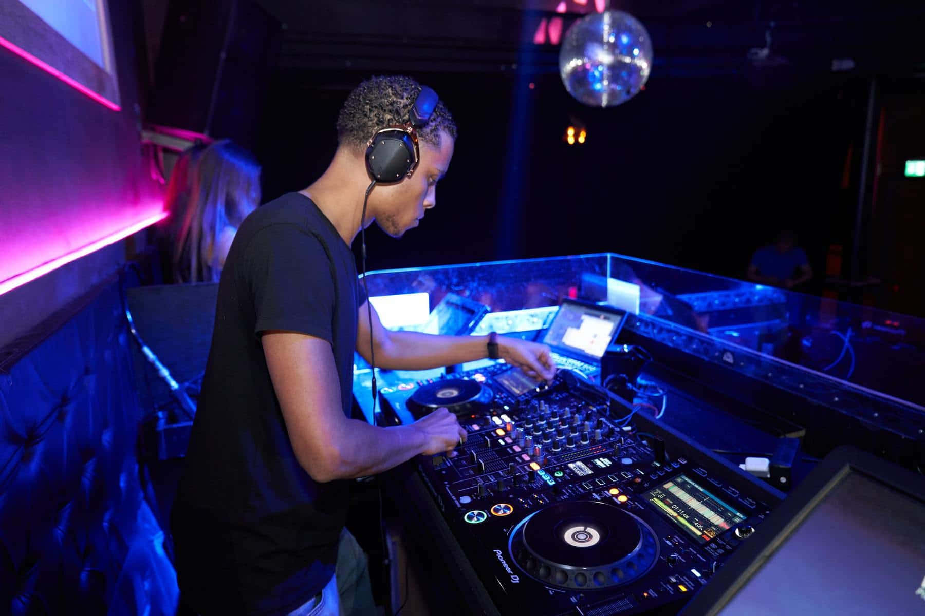 DJ 桌布 壁紙 — 一位戴著耳機的DJ在閃爍藍光的夜總會DJ台和迪斯科球下混合音樂。