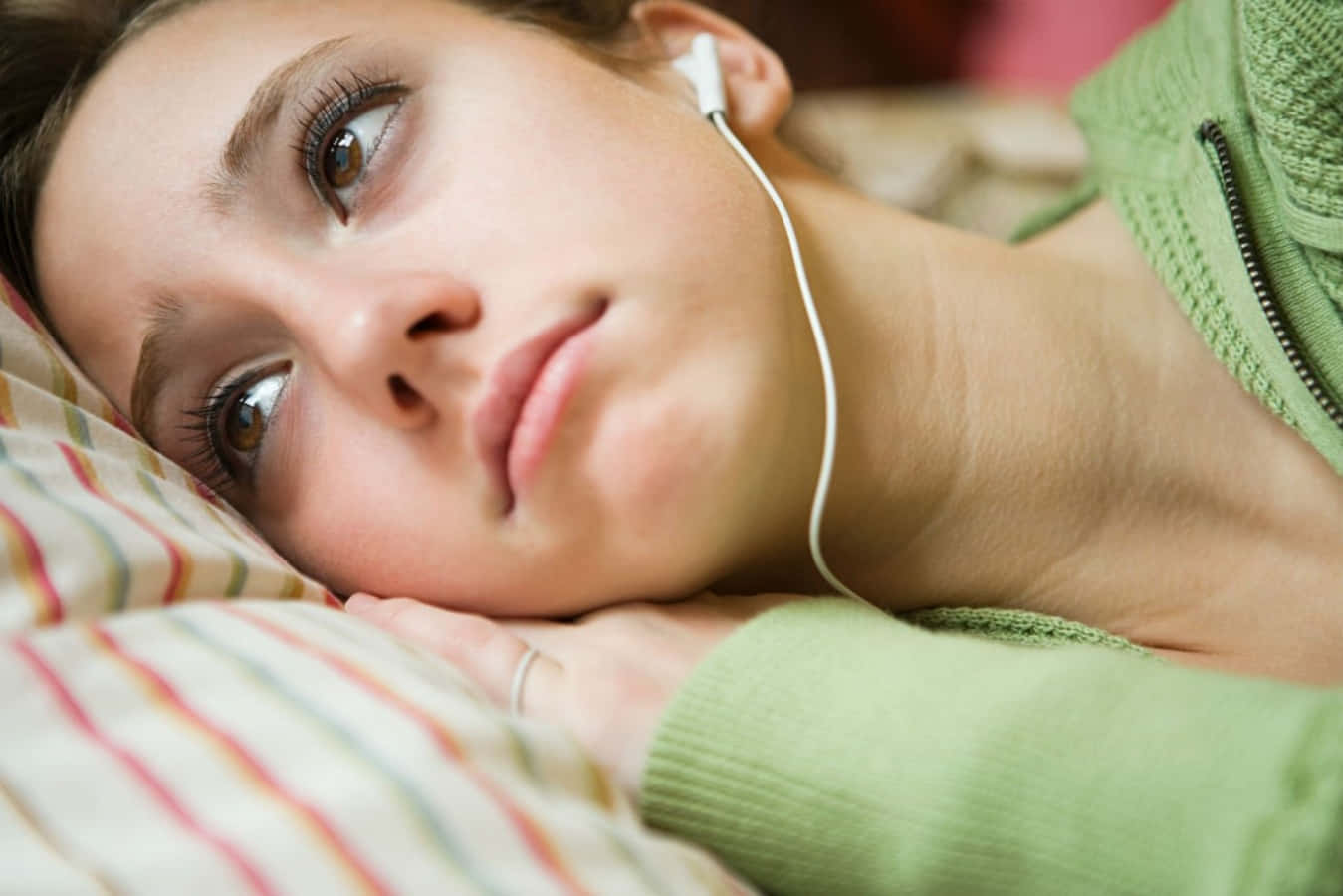 Emotional 桌布 壁紙 — 一位戴著耳機的年輕女子將頭靠在條紋枕頭上，向上凝視，表情若有所思。