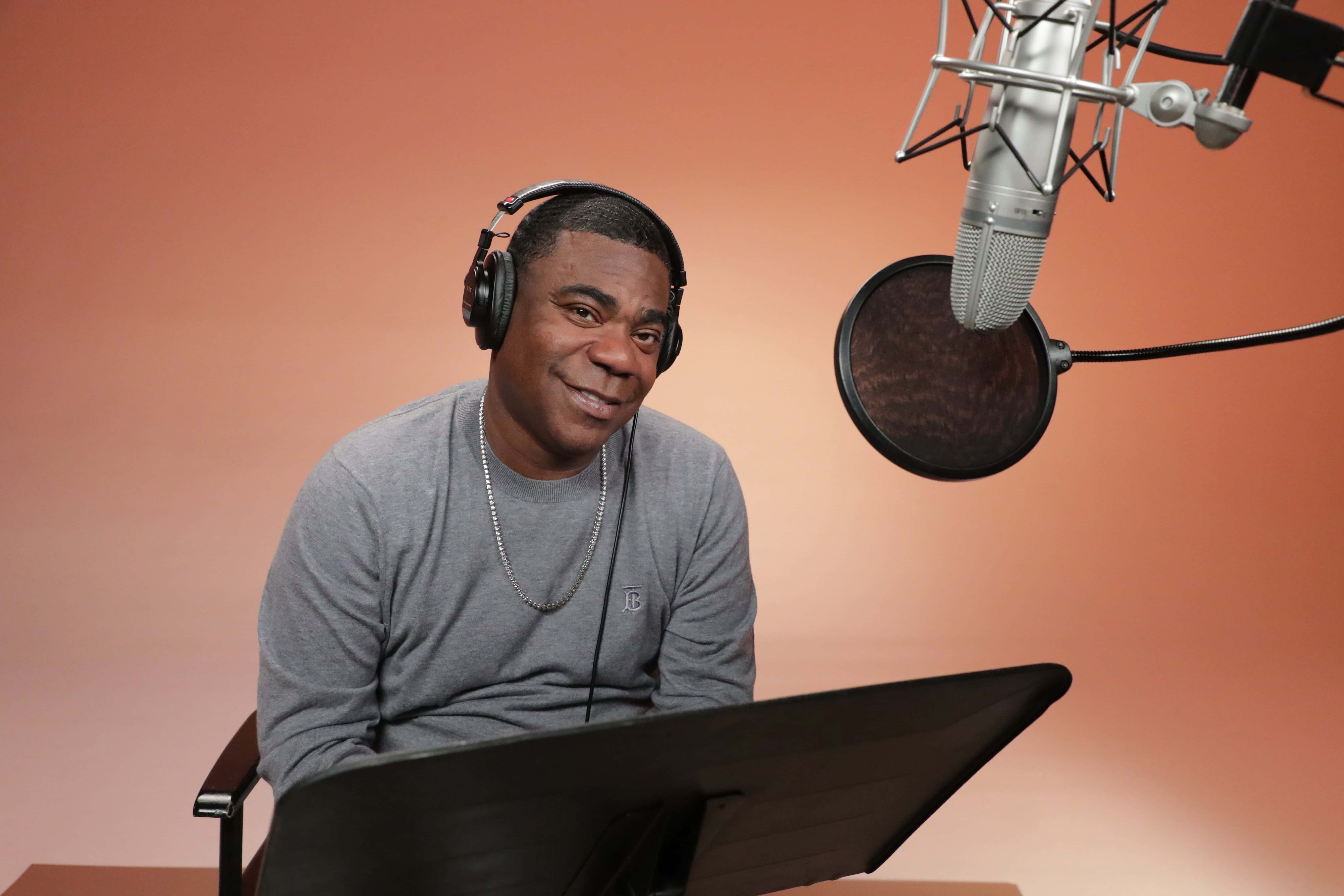 Tracy Morgan 桌布 壁紙 — 一位戴著耳機的微笑男子坐在錄音室麥克風前，背景為溫暖的橙色。