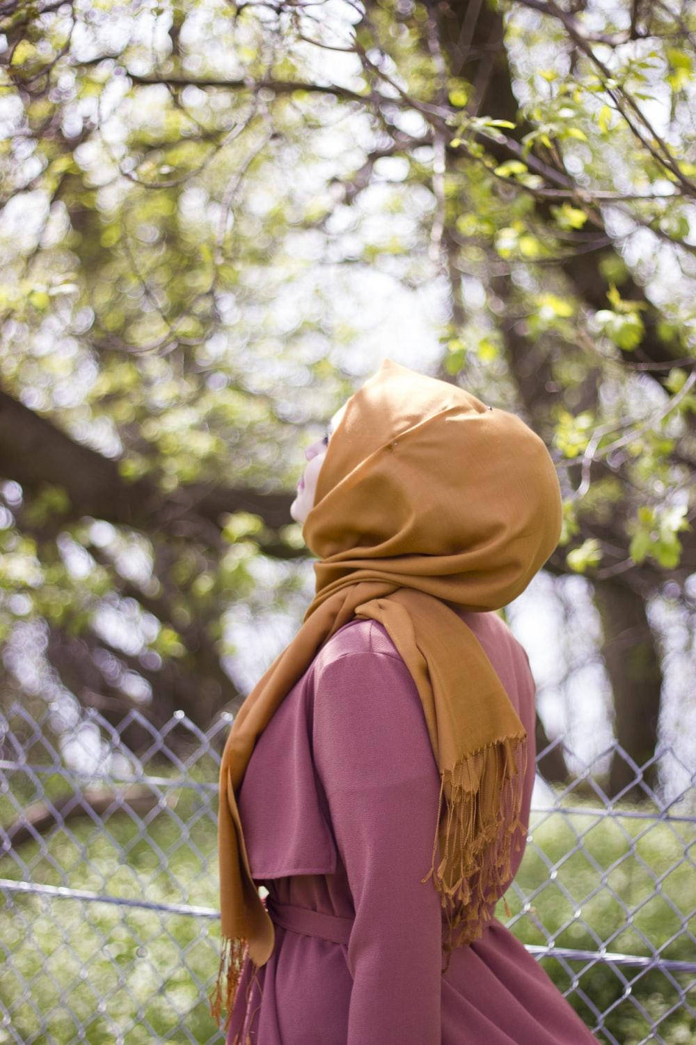 muslim 桌布 壁紙 — 一位戴著芥末黃頭巾和穿著淡紫色外套的女性，透過陽光普照、長滿嫩芽的樹冠向上凝望。