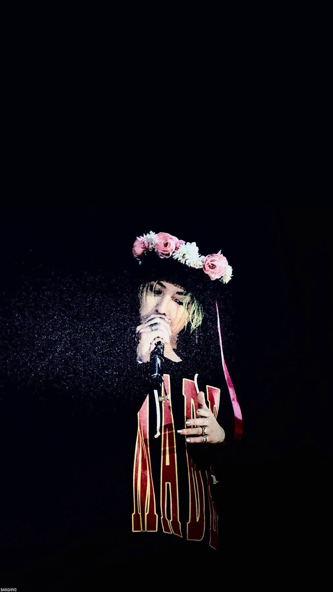G-dragon 桌布 壁紙 — 一位戴著花冠的表演者在黑色背景的舞台燈光下對著麥克風唱歌。