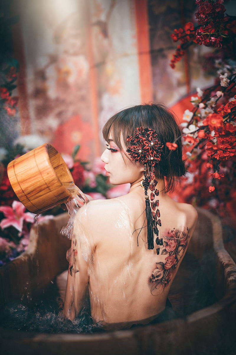 Tattoo 桌布 壁紙 — 一位戴著花卉頭飾和玫瑰刺青的女士，正將木桶中的水倒入一個被紅花環繞的木盆中。