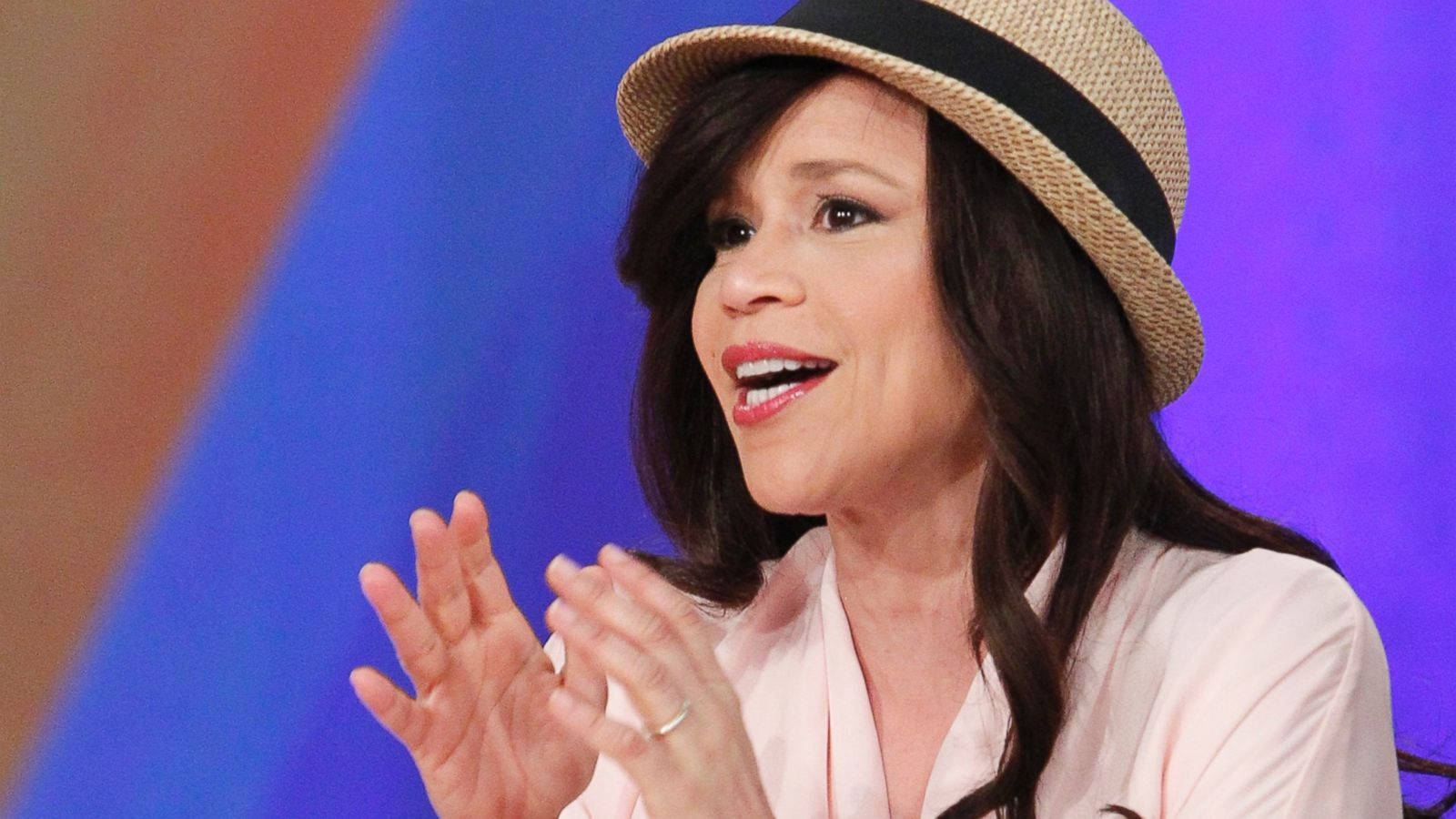 Celebrity 桌布 壁紙 — 一位戴著草帽、身穿粉紅色襯衫的女性，在充滿活力的藍色和橙色漸變背景前生動地做著手勢。