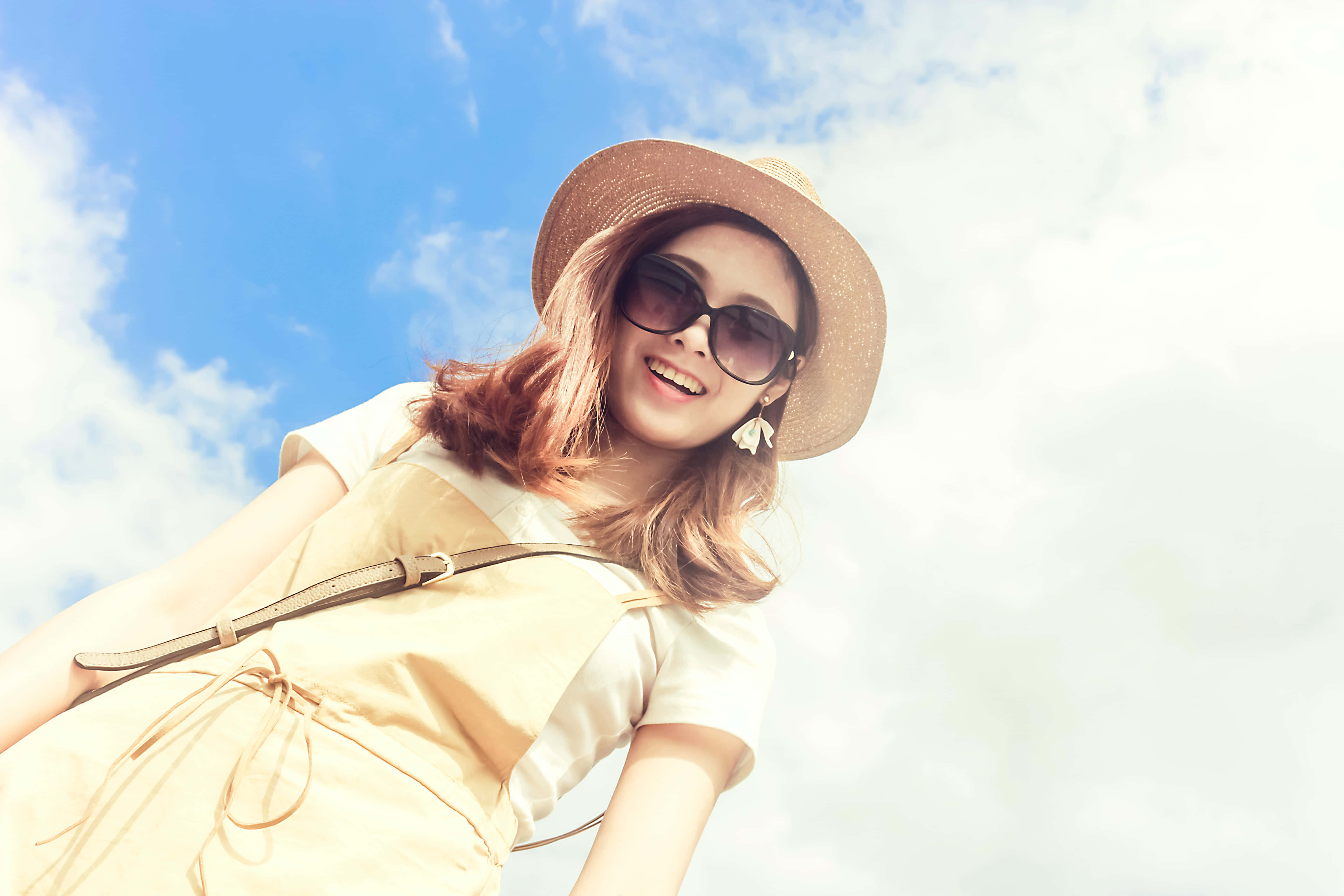 Summer Fashion 桌布 壁紙 — 一位戴著草帽和太陽眼鏡的微笑女士，在藍天白雲下大笑。