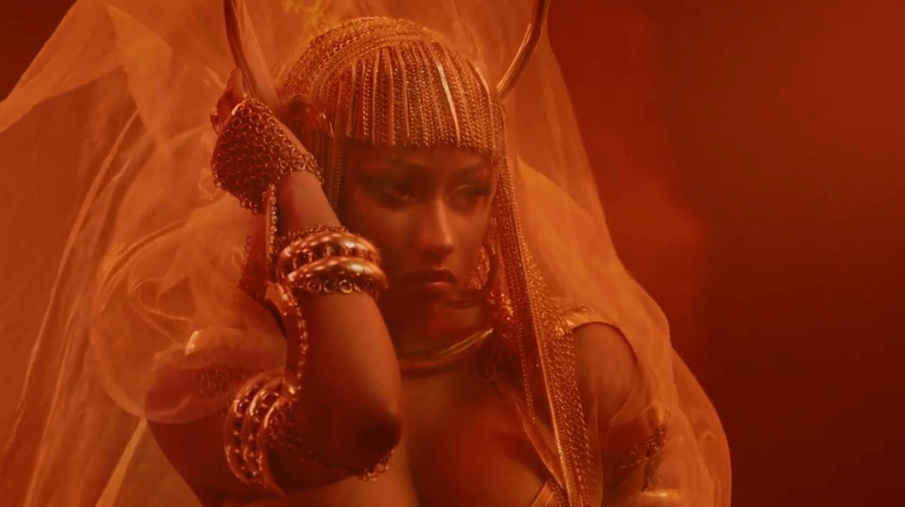 Nicki 桌布 壁紙 — 一位戴著華麗金色頭飾和珠寶的女性，在朦朧的橙色背景下，戴著面紗擺姿勢。