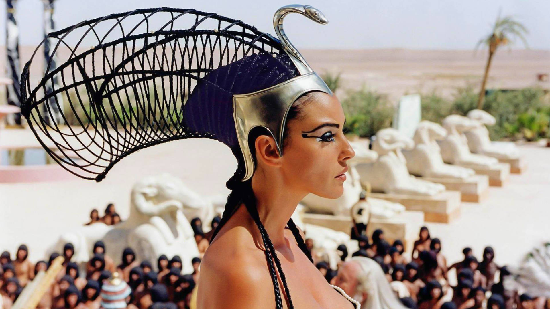 Cleopatra 桌布 壁紙 — 一位戴著華麗銀黑色頭飾的女性，在沙漠環境中莊嚴地站在獅身人面像雕像前。