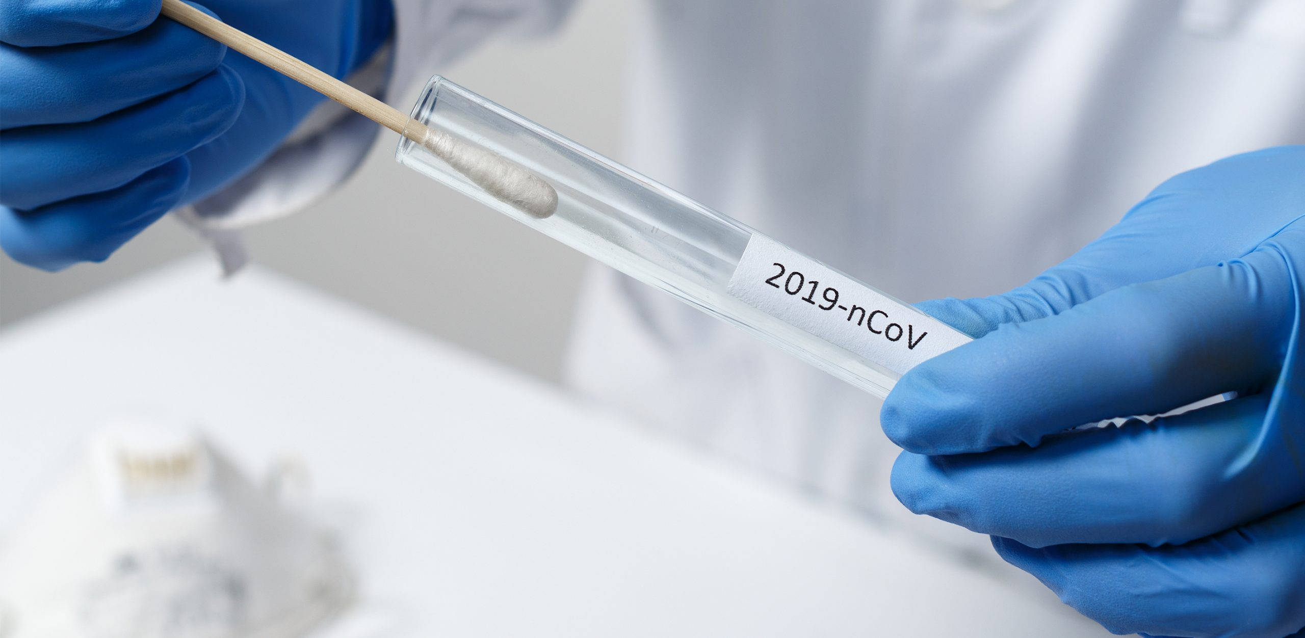 Covid 桌布 壁紙 — 一位戴著藍色手套的科學家將拭子插入一個標有2019-nCoV的試管中，放在實驗室工作台上。