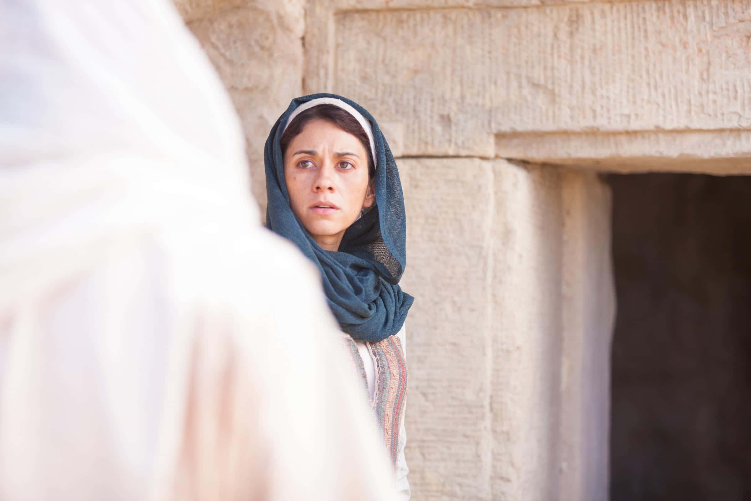 Mary Magdalene 桌布 壁紙 — 一位戴著藍色頭巾的女性，專注地凝視著古老石頭遺跡前一個模糊的身影。