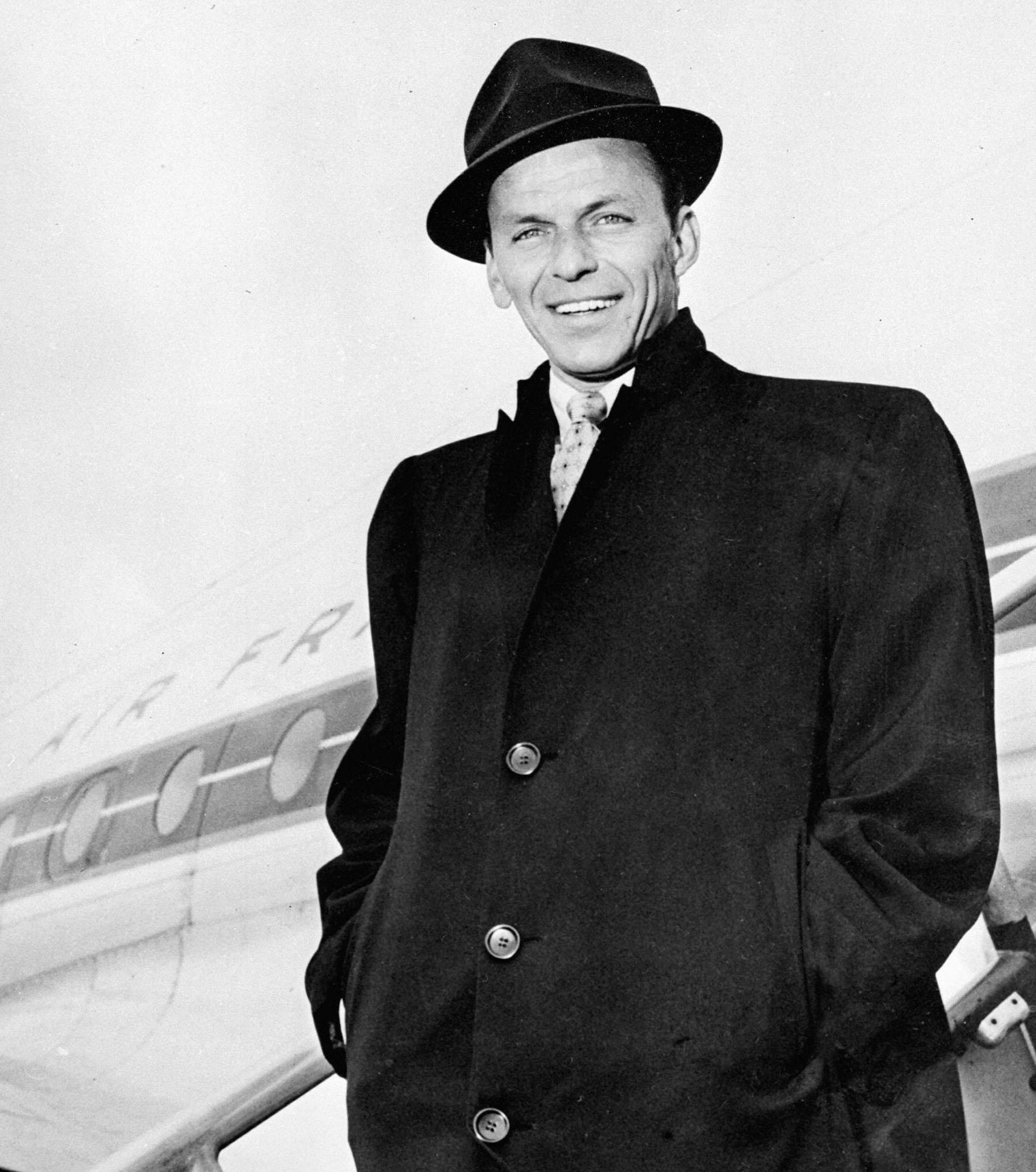 Sinatra 桌布 壁紙 — 一位戴著軟呢帽和外套的微笑男子自信地站在飛機旁邊，這是一張經典的黑白照片。