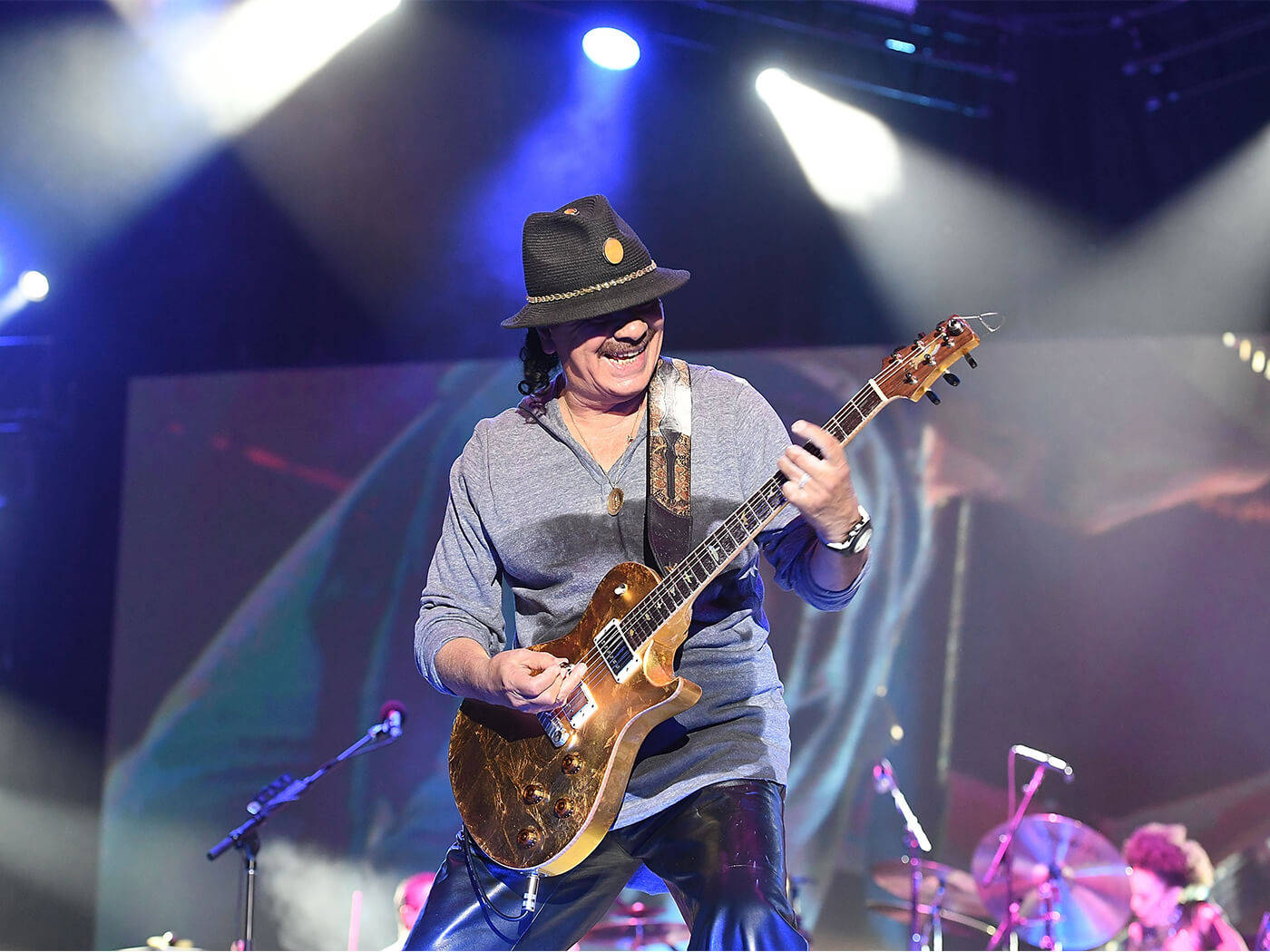 guitar player 桌布 壁紙 — 一位戴著軟呢帽的快樂吉他手，在現場音樂會中，於充滿活力的舞台燈光下彈奏一把旭日漸變色電吉他。