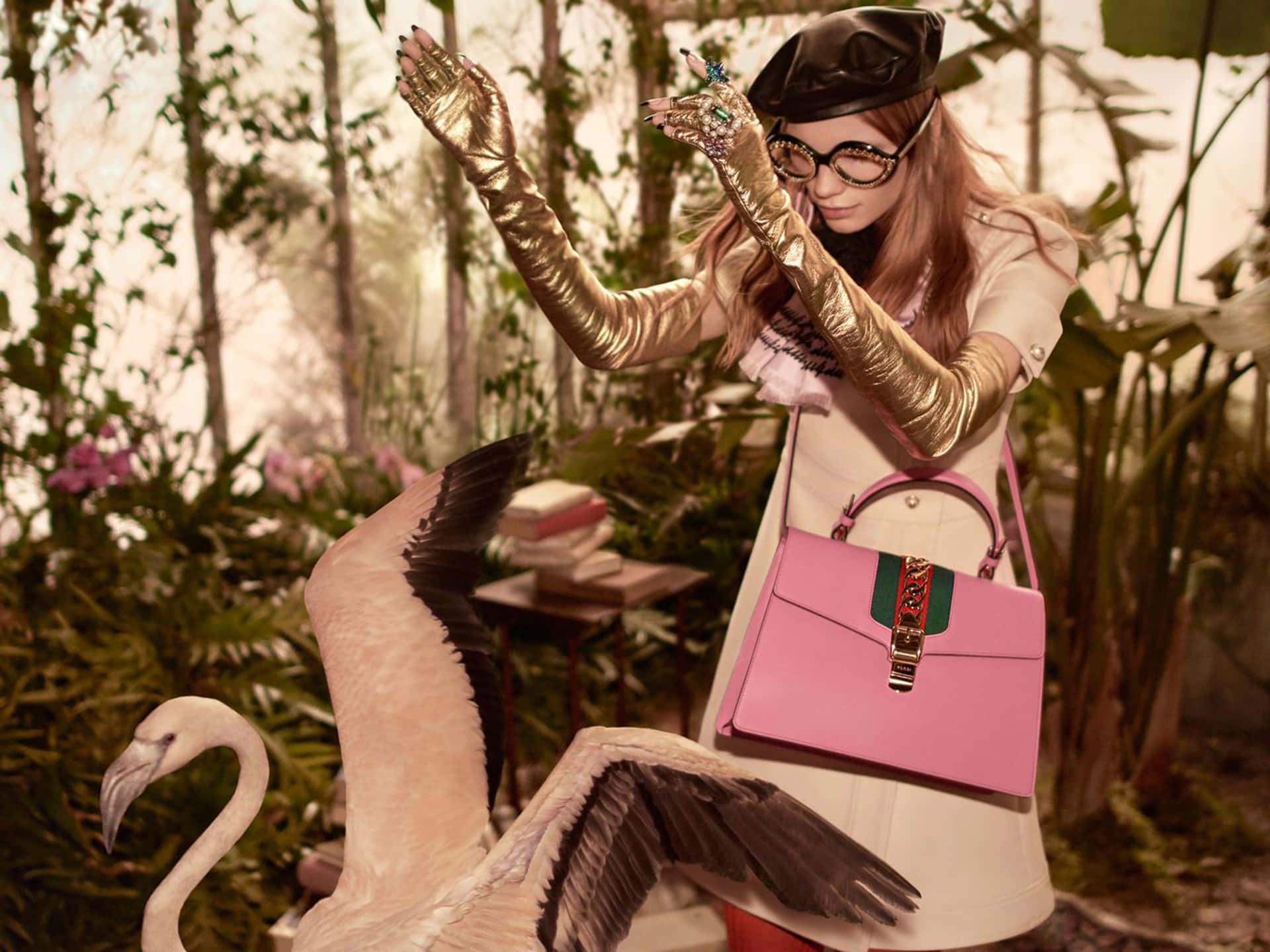 戴著金色手套和粉色手提袋的女性在熱帶溫室中與紅鶴一起。 — Gucci GIF 壁紙