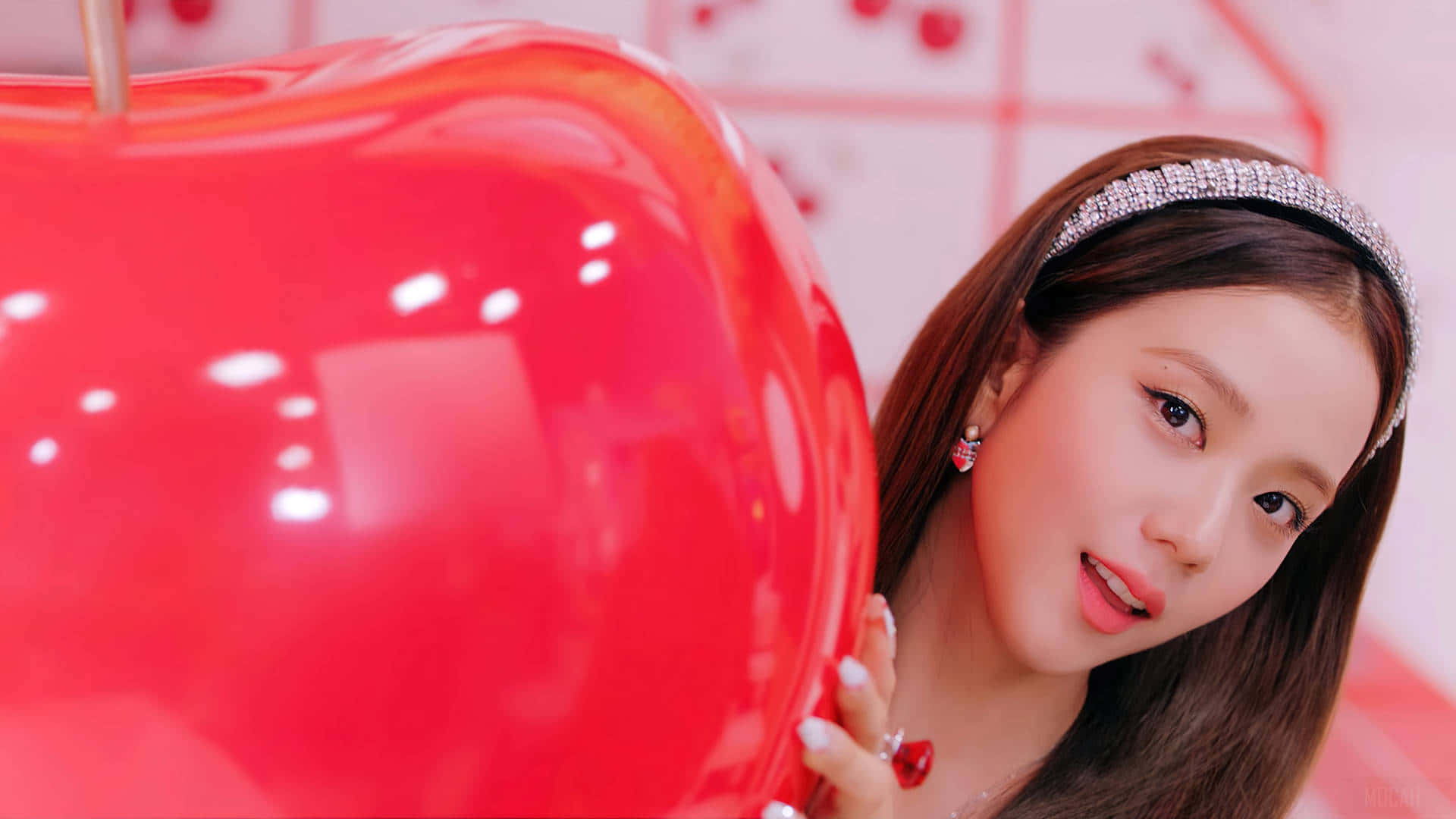 BLACKPINK 桌布 壁紙 — 一位戴著鑲寶石頭帶的年輕女性，在明亮的粉紅色背景中，從一個巨大的光澤紅蘋果後面頑皮地探出頭來。