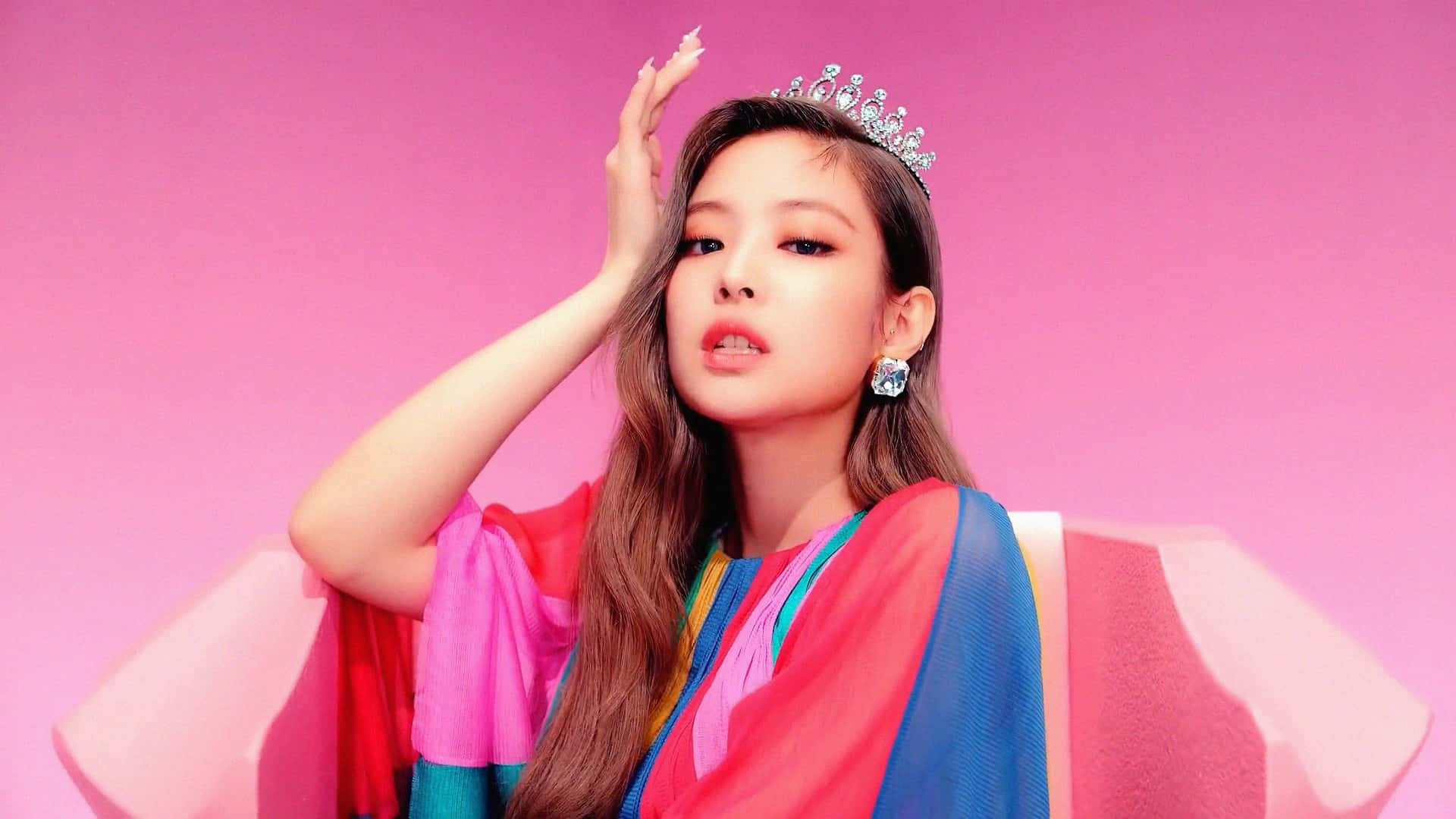 BLACKPINK 桌布 壁紙 — 一位戴著閃亮頭飾、身穿色彩繽紛層次服裝的女性，在充滿活力的粉紅色背景前自信地擺姿勢。