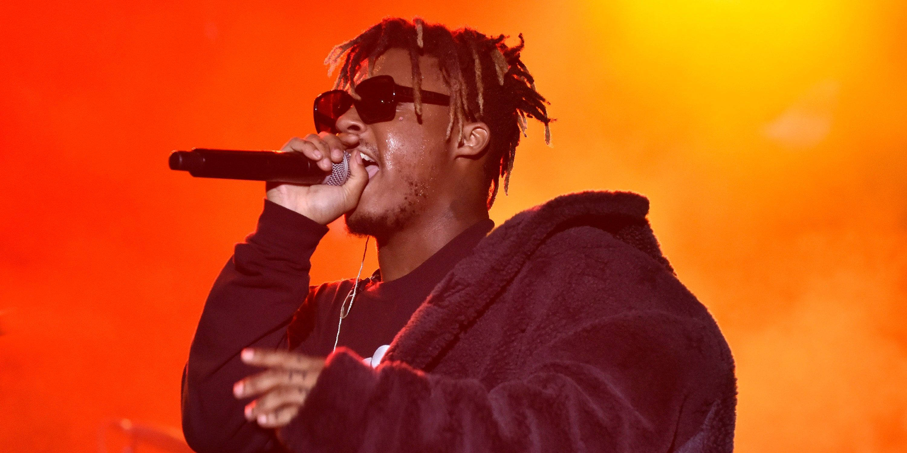 Juice Wrld Desktop 桌布 壁紙 — 一位戴著雷鬼辮和太陽眼鏡的饒舌歌手，在熾熱的橙色舞台燈光下，對著麥克風熱情表演。