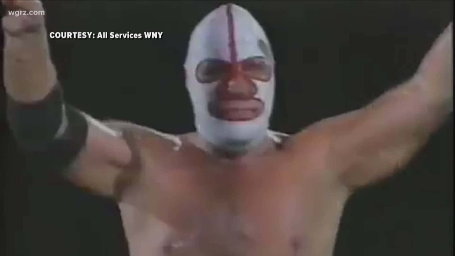 WWE 桌布 壁紙 — 一位戴著面具的摔角手，臉上塗有白色顏料和紅色標記，在黑暗背景下勝利地舉起雙臂。