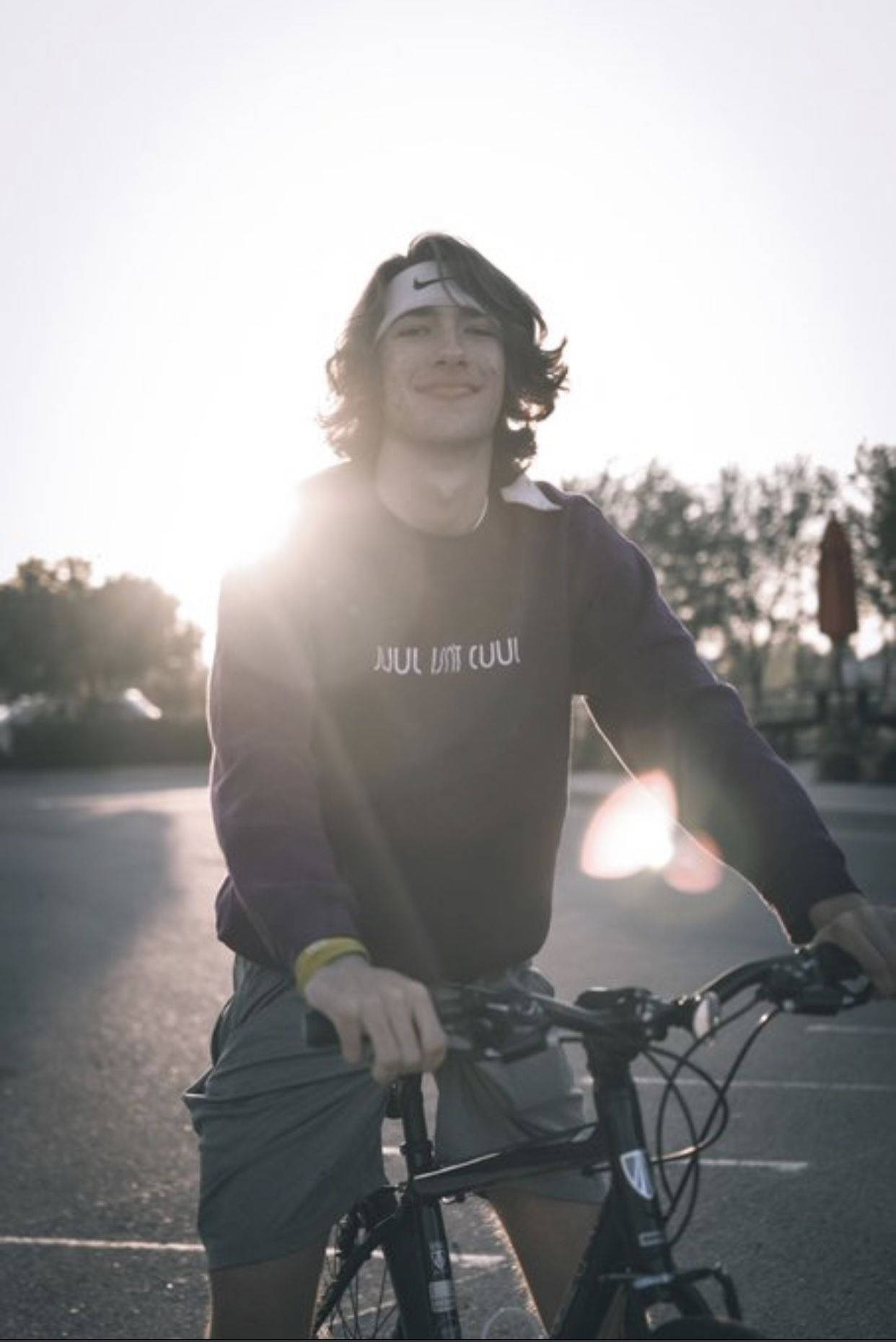 Baylen Levine 桌布 壁紙 — 一位戴著頭帶的年輕男子在陽光明媚的停車場中微笑著拿著一輛自行車，正值黃金時刻。