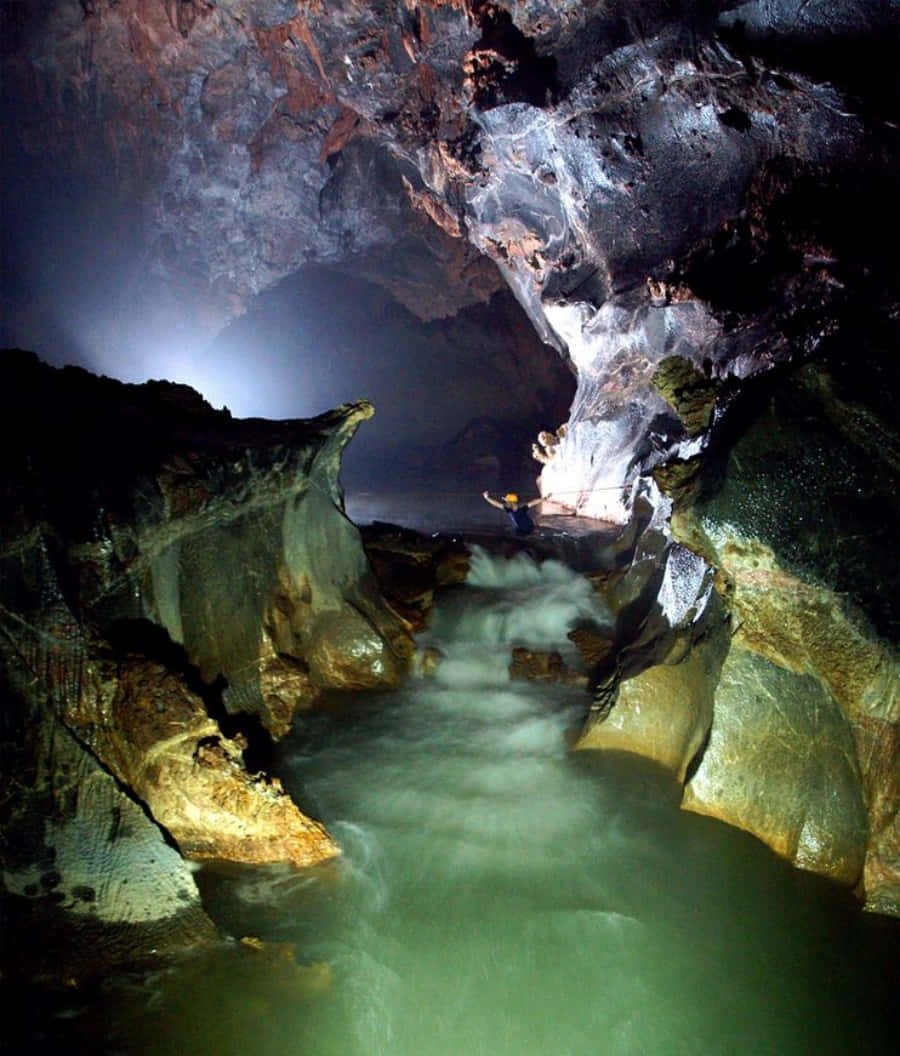 Cave 桌布 壁紙 — 一位戴著頭盔的洞穴探險家探索一個戲劇性的洞穴，發光的綠色水流經崎嶇的岩石結構。
