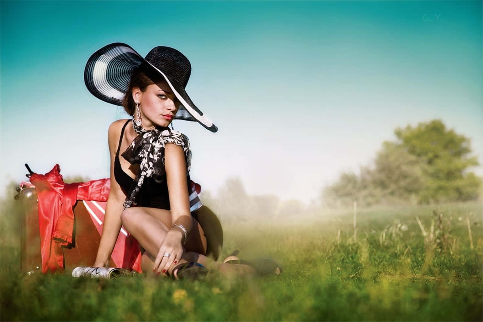 Spring Fashion 桌布 壁紙 — 一位戴著黑色帽子、身穿紅色外套的時尚女性，優雅地坐在陽光明媚、背景迷濛的草地上。
