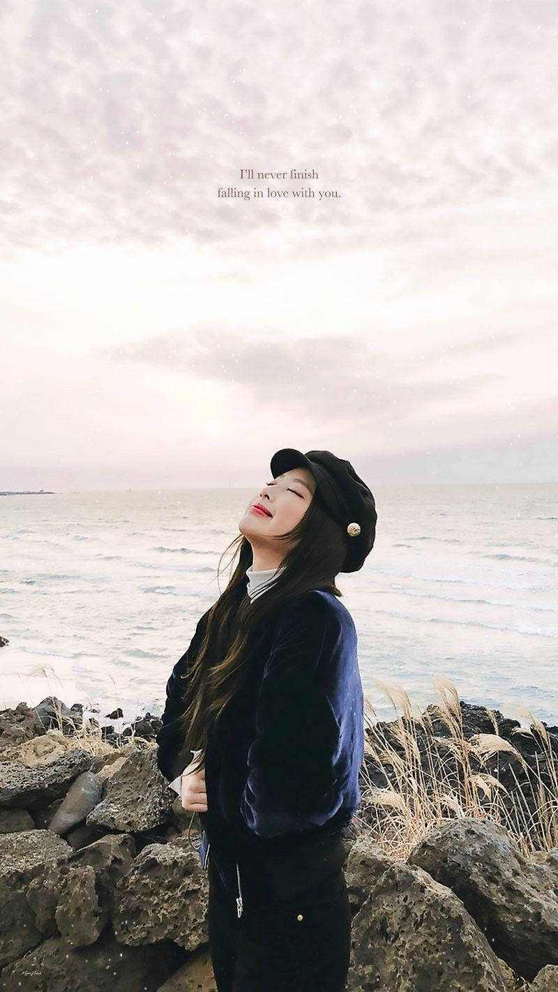 Jennie 桌布 壁紙 — 一位戴著黑色貝雷帽、穿著天鵝絨外套的年輕女子，平靜地站在岩石海邊懸崖上，閉著眼睛，溫柔的海浪在柔和的多雲天空下翻滾。