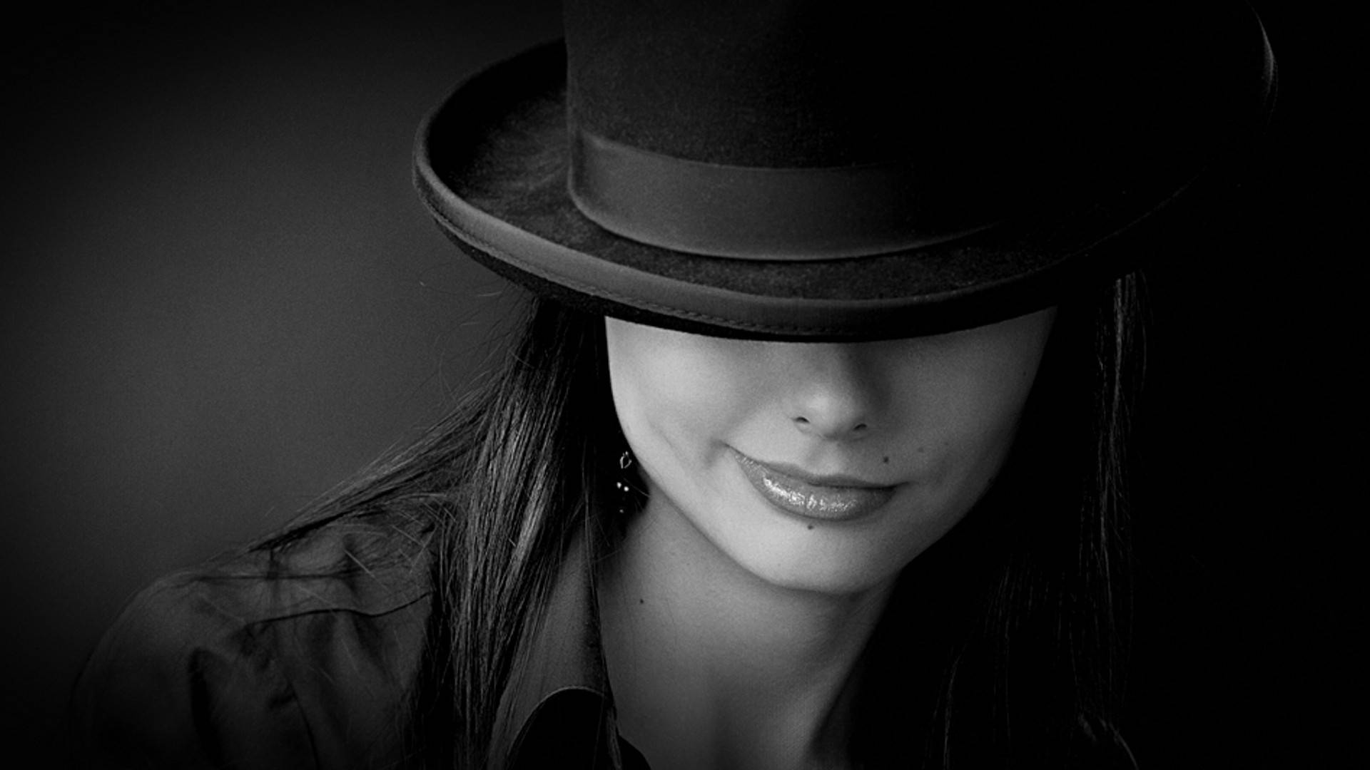 Egocentric 桌布 壁紙 — 一位戴著黑色高帽的女性在陰鬱的黑白肖像中微笑，她的臉部部分被陰影遮蓋。