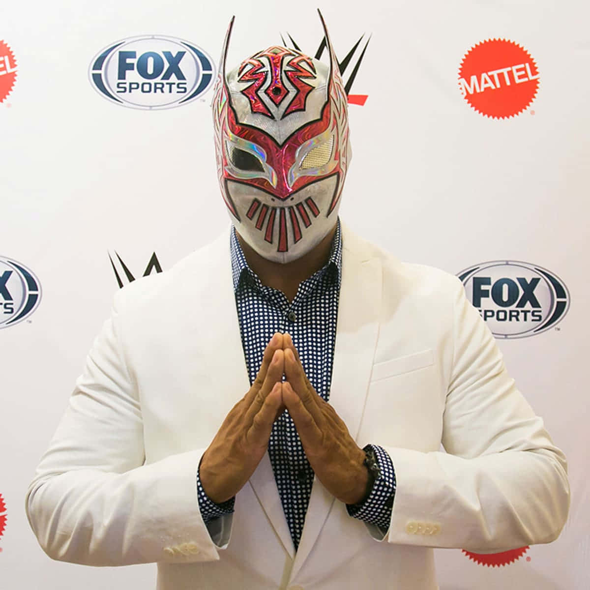 WWE 桌布 壁紙 — 一位戴面具的摔角手身穿白色西裝和格子襯衫，雙手合十站在品牌背景前。