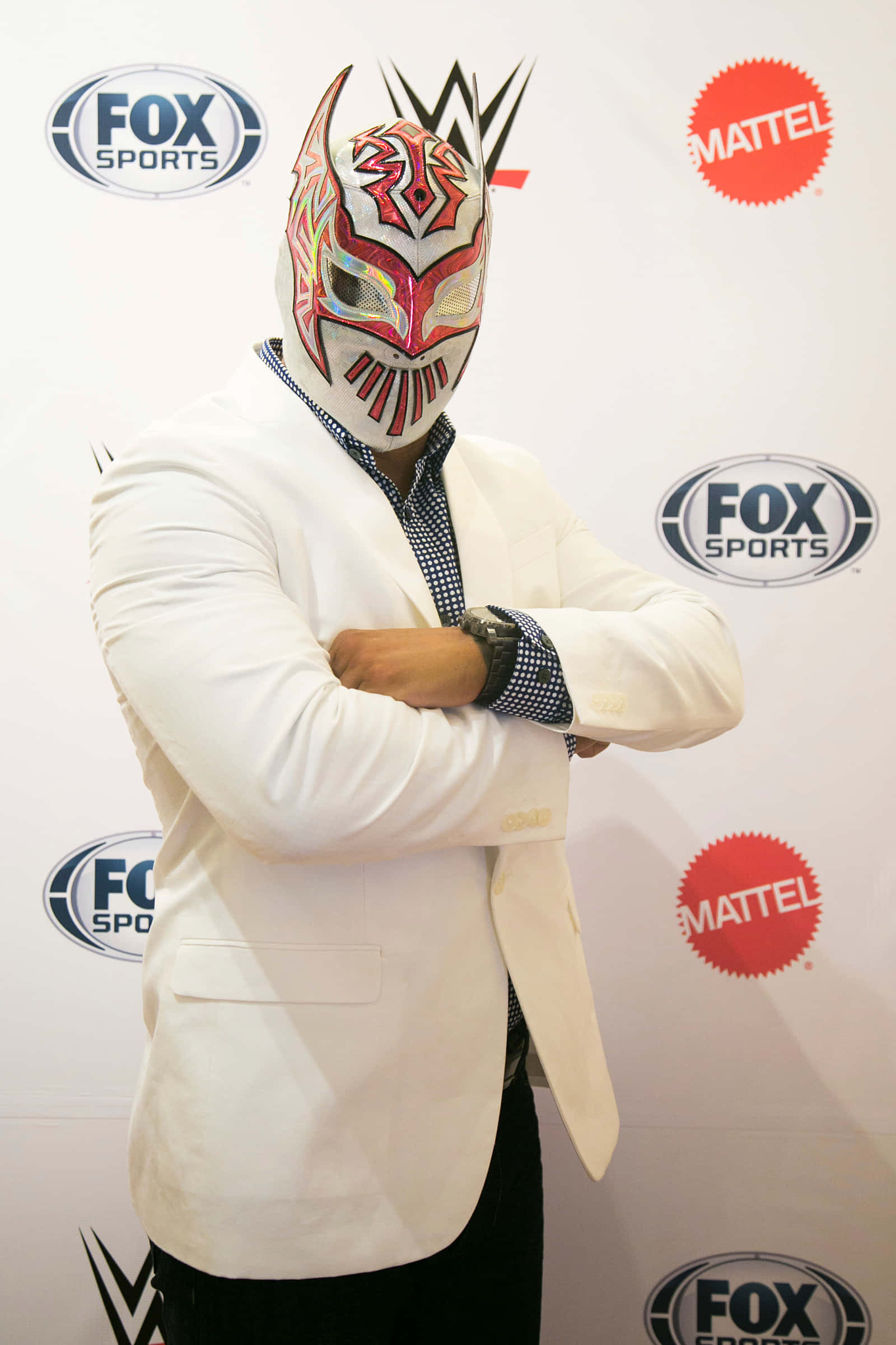 WWE 桌布 壁紙 — 一位戴面具的摔角手身穿白色西裝外套，雙臂交叉，自信地站在品牌活動背景前。