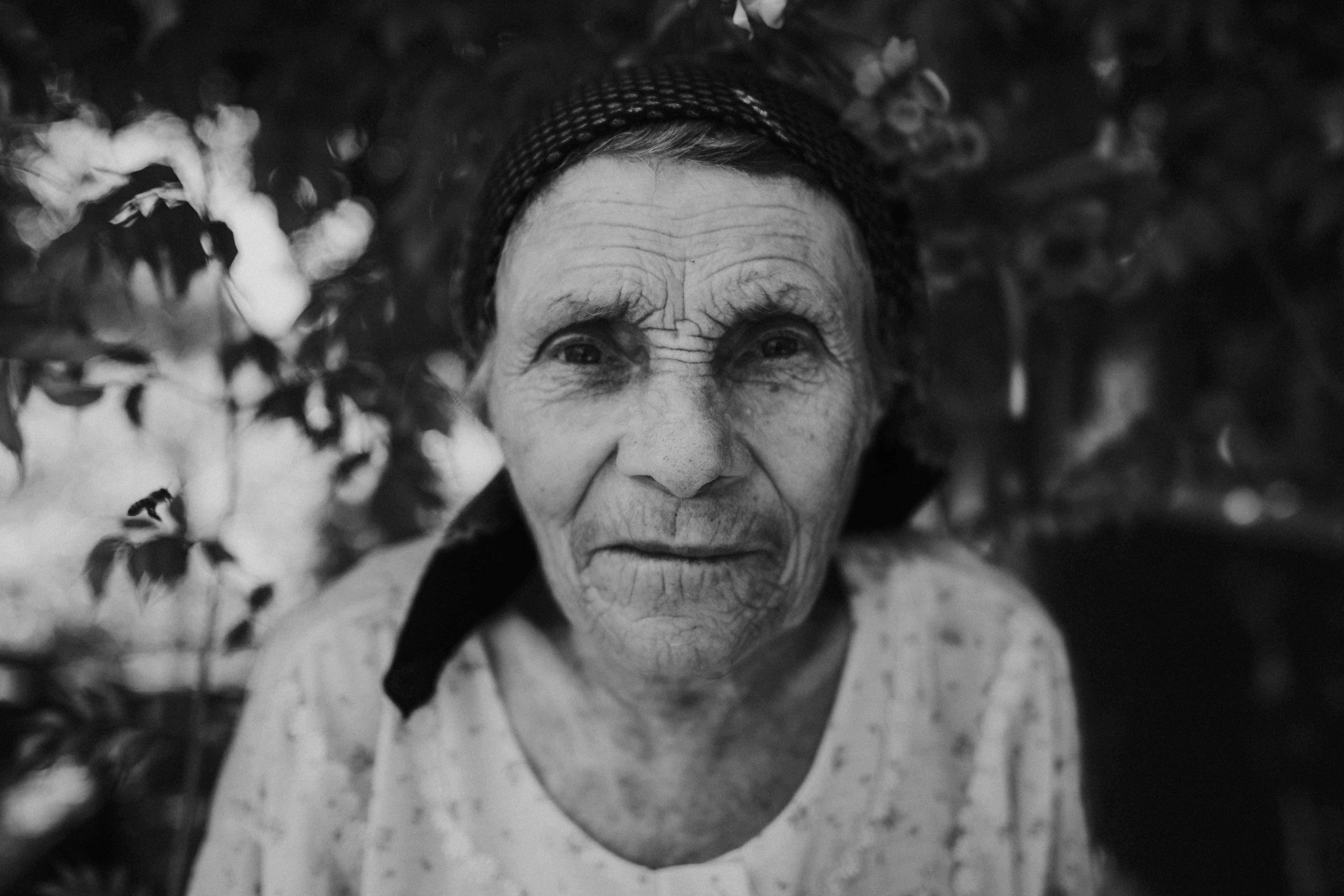 Mature 桌布 壁紙 — 一位戴頭巾、滿臉皺紋的老婦人的黑白特寫肖像，背景是模糊的樹葉。