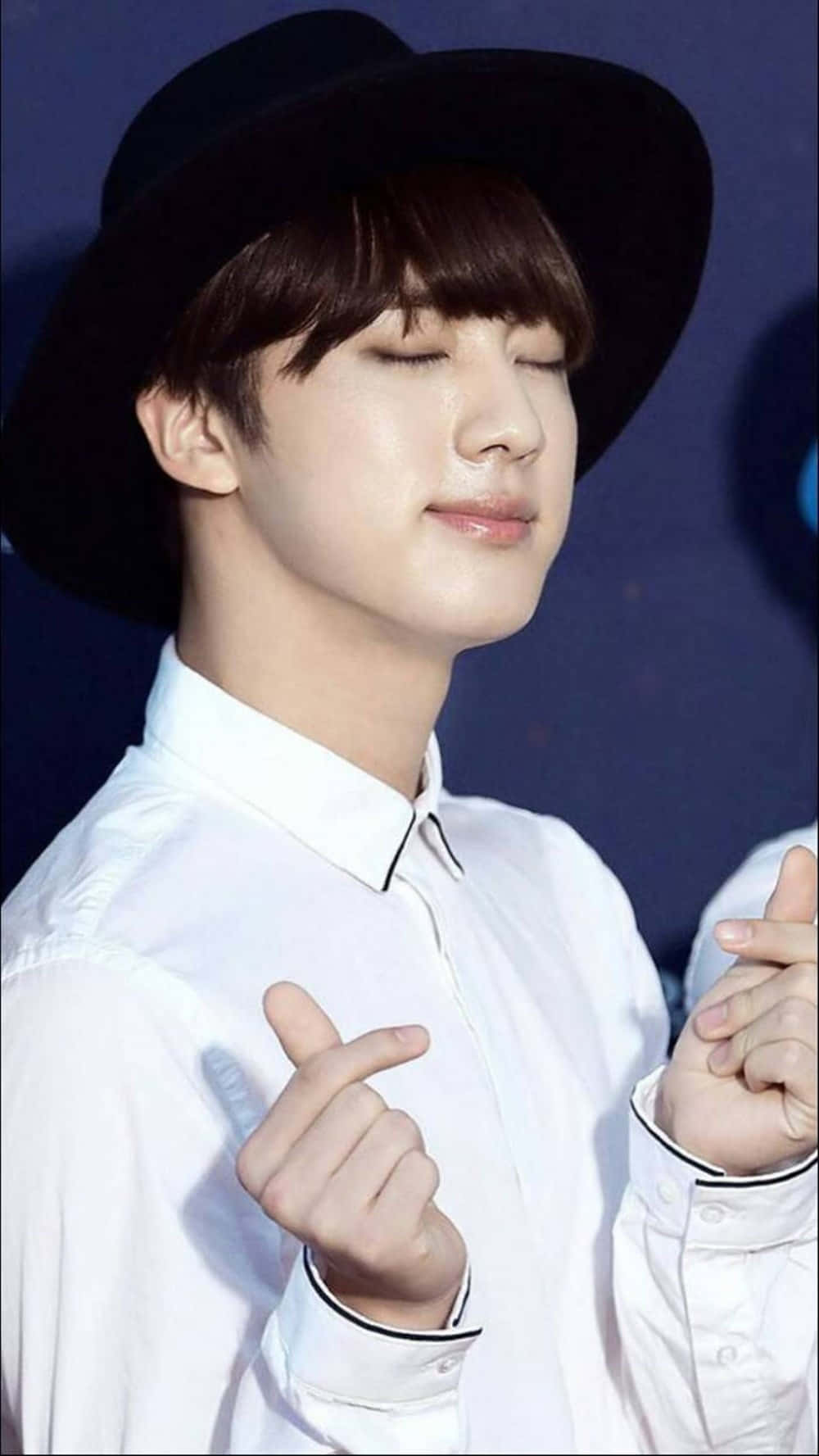 BTS 桌布 壁紙 — 一位戴黑色帽子和穿白色襯衫的年輕男子閉著眼睛微笑，同時做出手指愛心手勢。